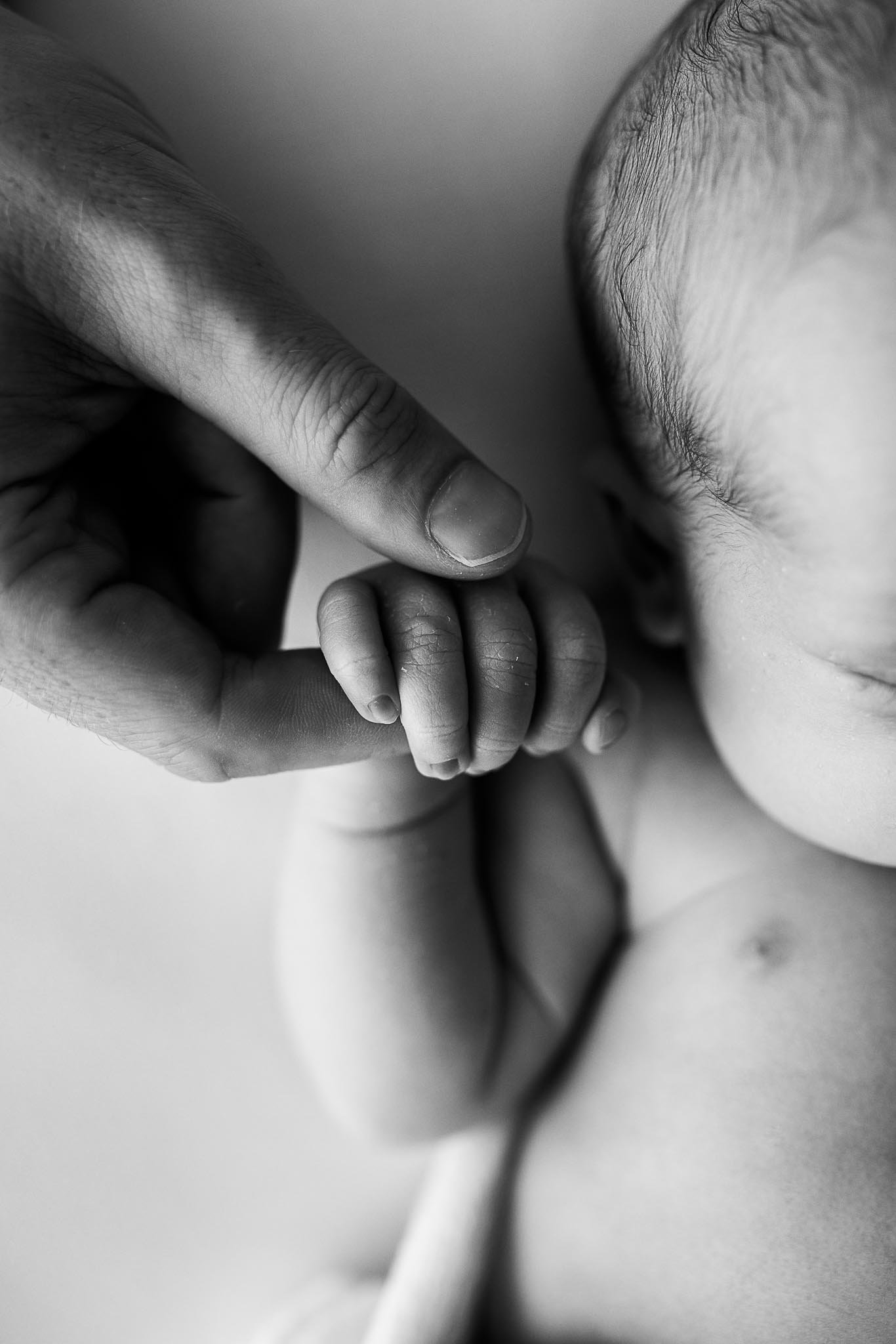 Black and white close-up photo of an adult holding the hand of a small child or baby.