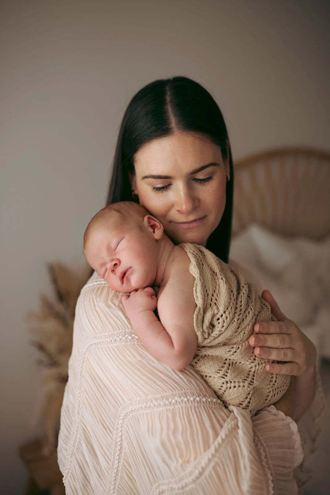A woman with black hair holding a sleeping baby with reddish hair on her shoulder, in a cozy room.