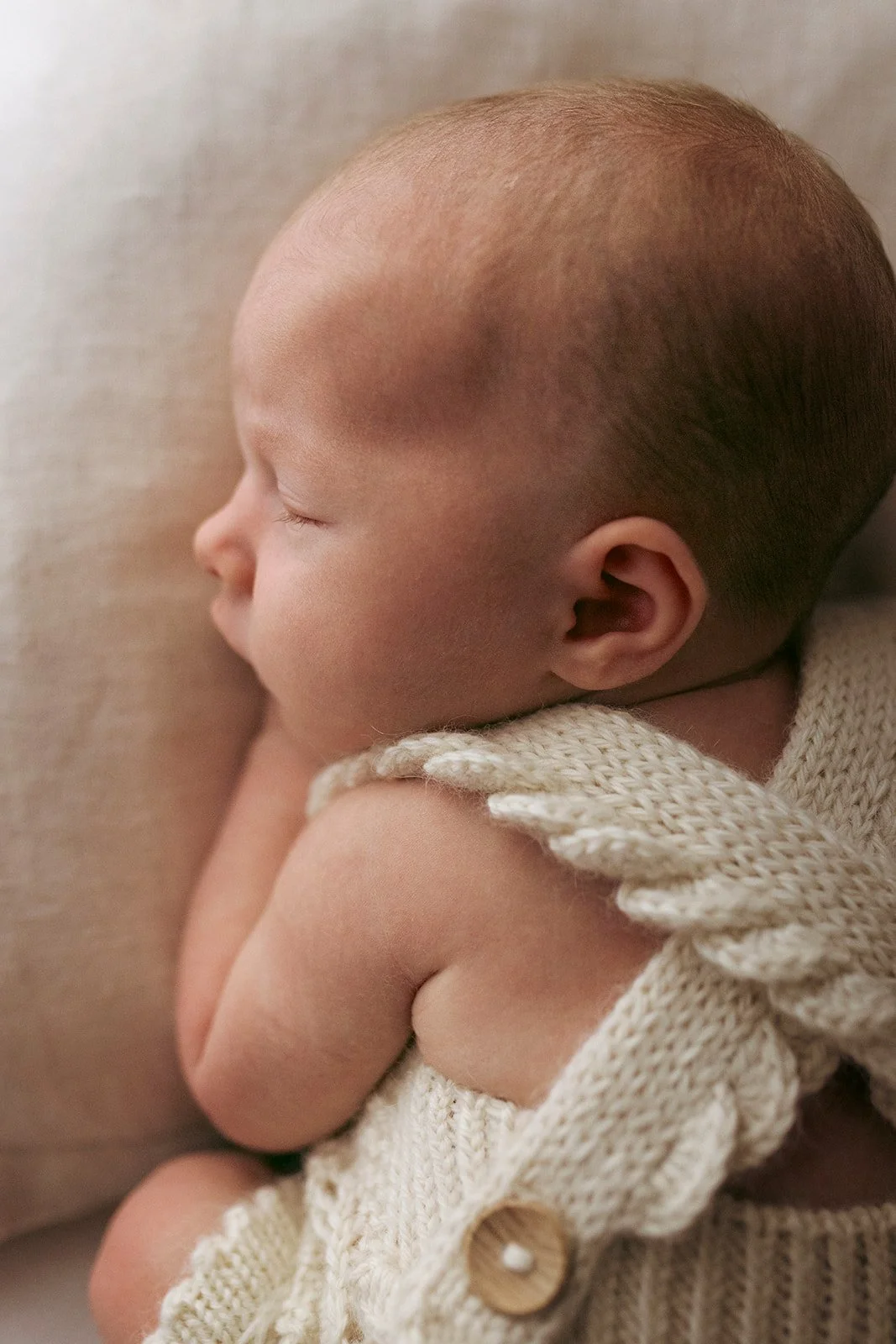 Side view of a sleeping infant with a knit sweater, lying on a soft surface.