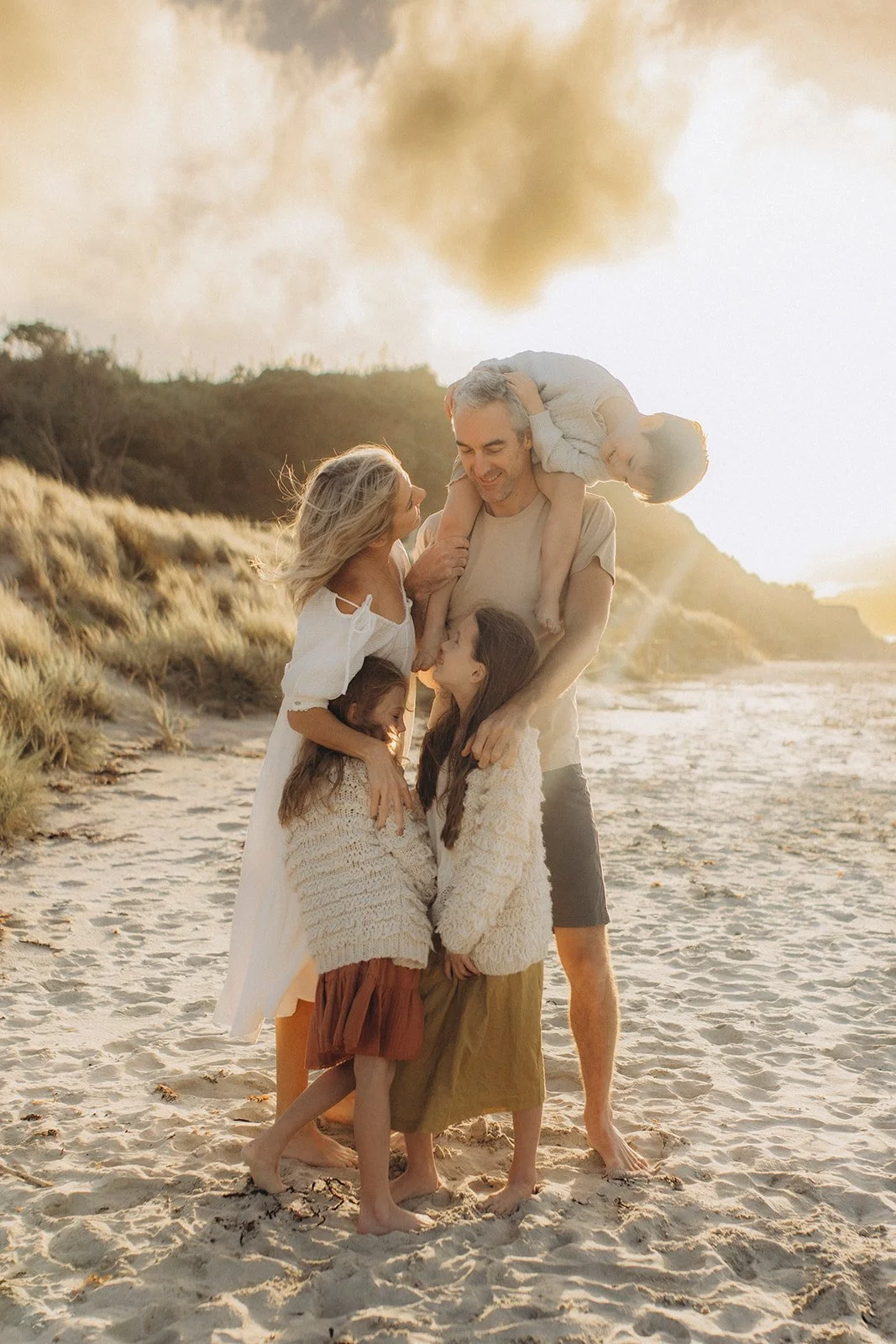 A family of five enjoying time on the beach at sunset, with smoke in the background.