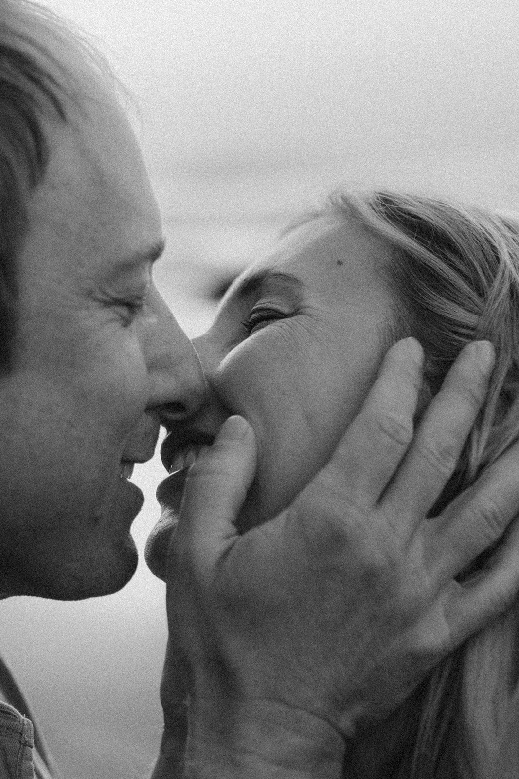 A black and white close-up photo of a man and woman sharing a kiss, with the man's face on the left and the woman's face on the right, holding her face gently.