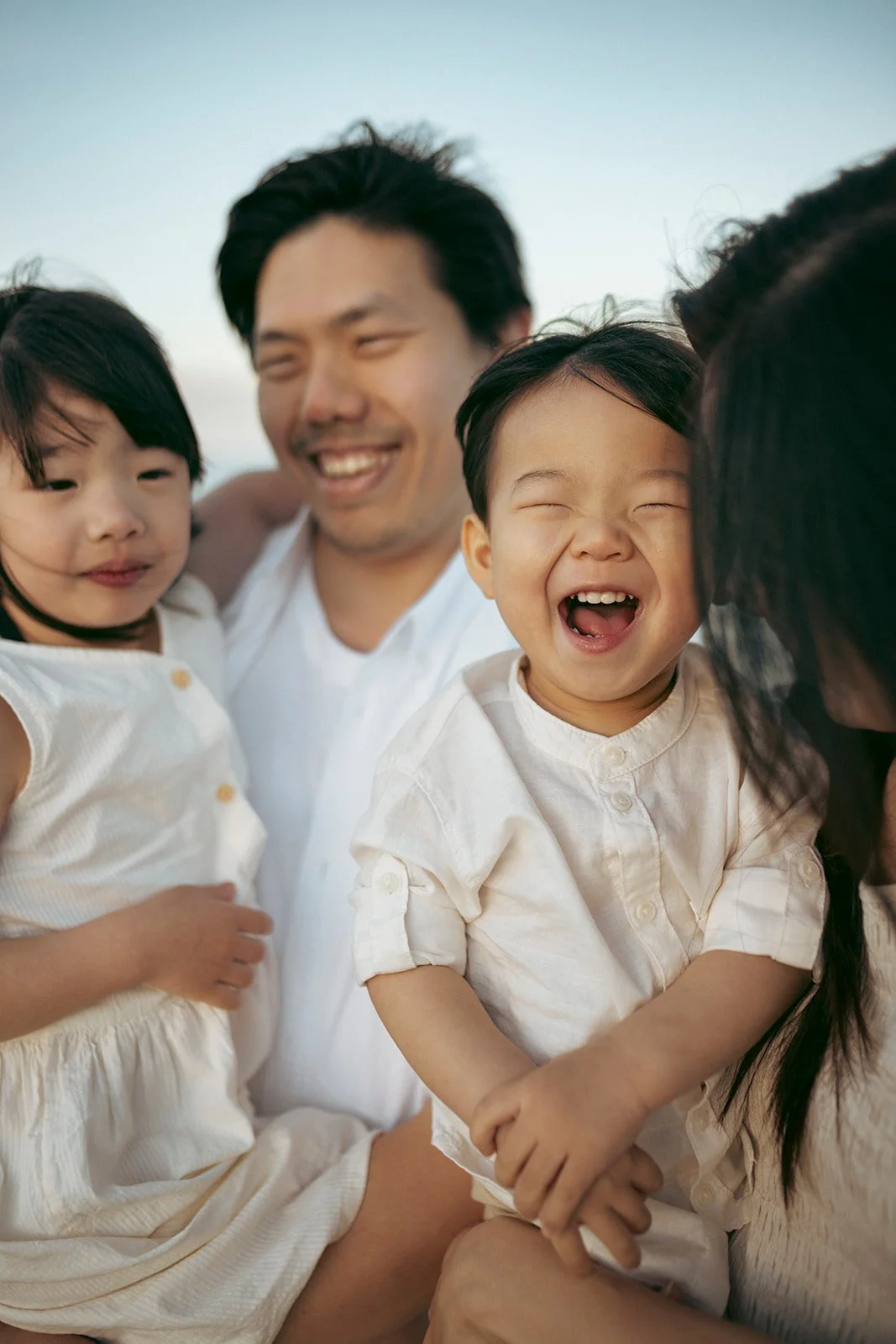 A happy man holding two young children, all smiling and enjoying time together outdoors.
