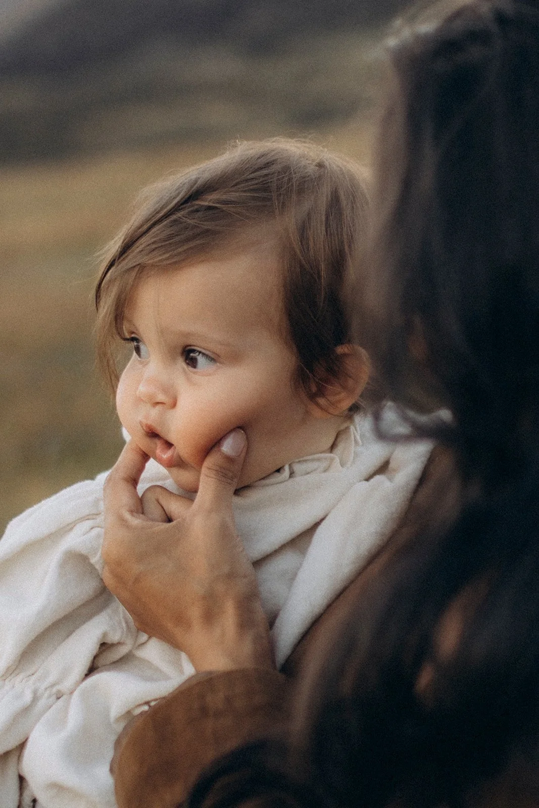 A close-up of a young child with brown hair and blue eyes, being gently touched on the face by an adult's hand. The child appears to be deep in thought.