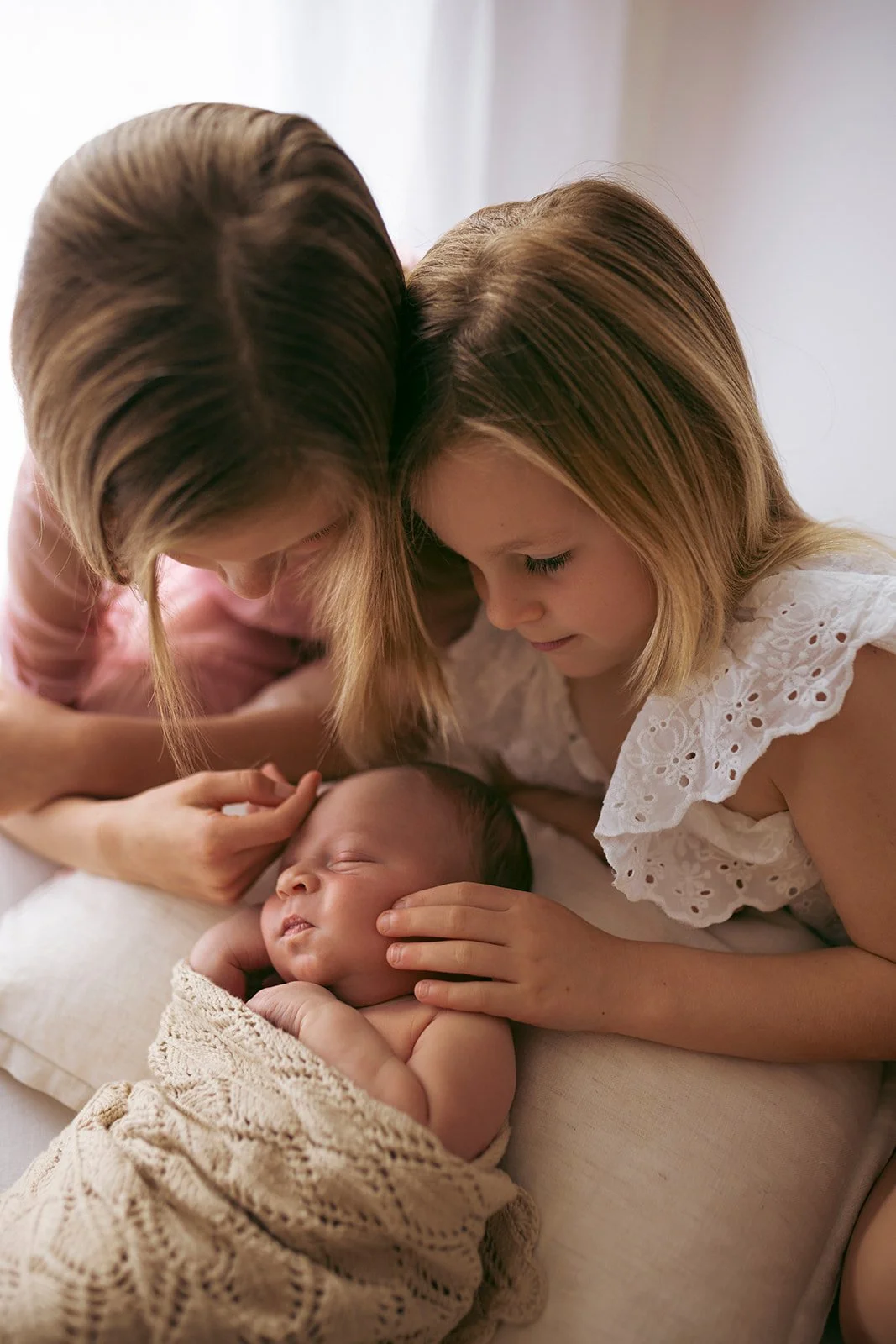 A woman and a girl are gently holding a sleeping baby, touching its head and face with tender affection.