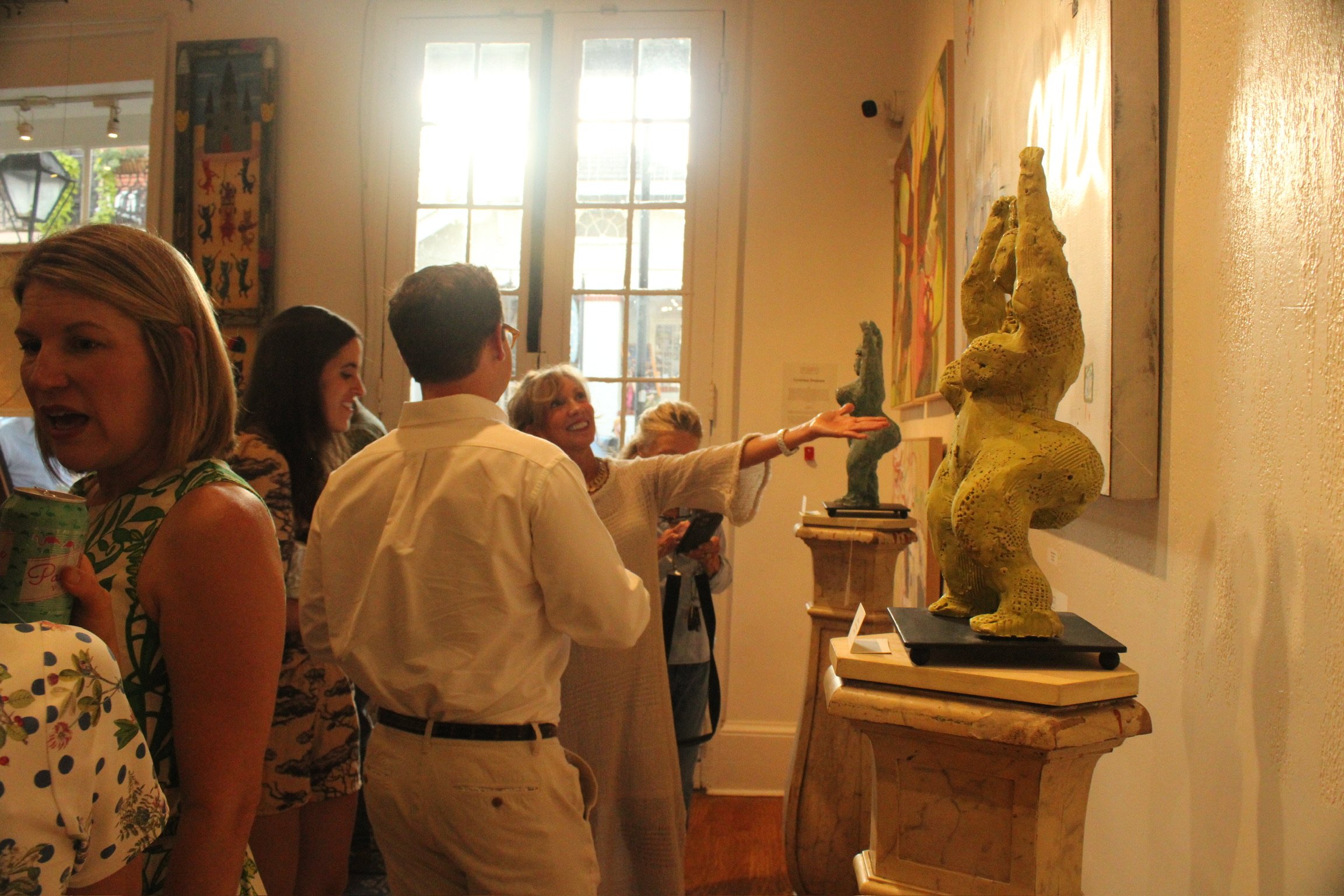 People viewing sculptures of fantasy creatures in an art gallery with artwork on the walls and large windows.