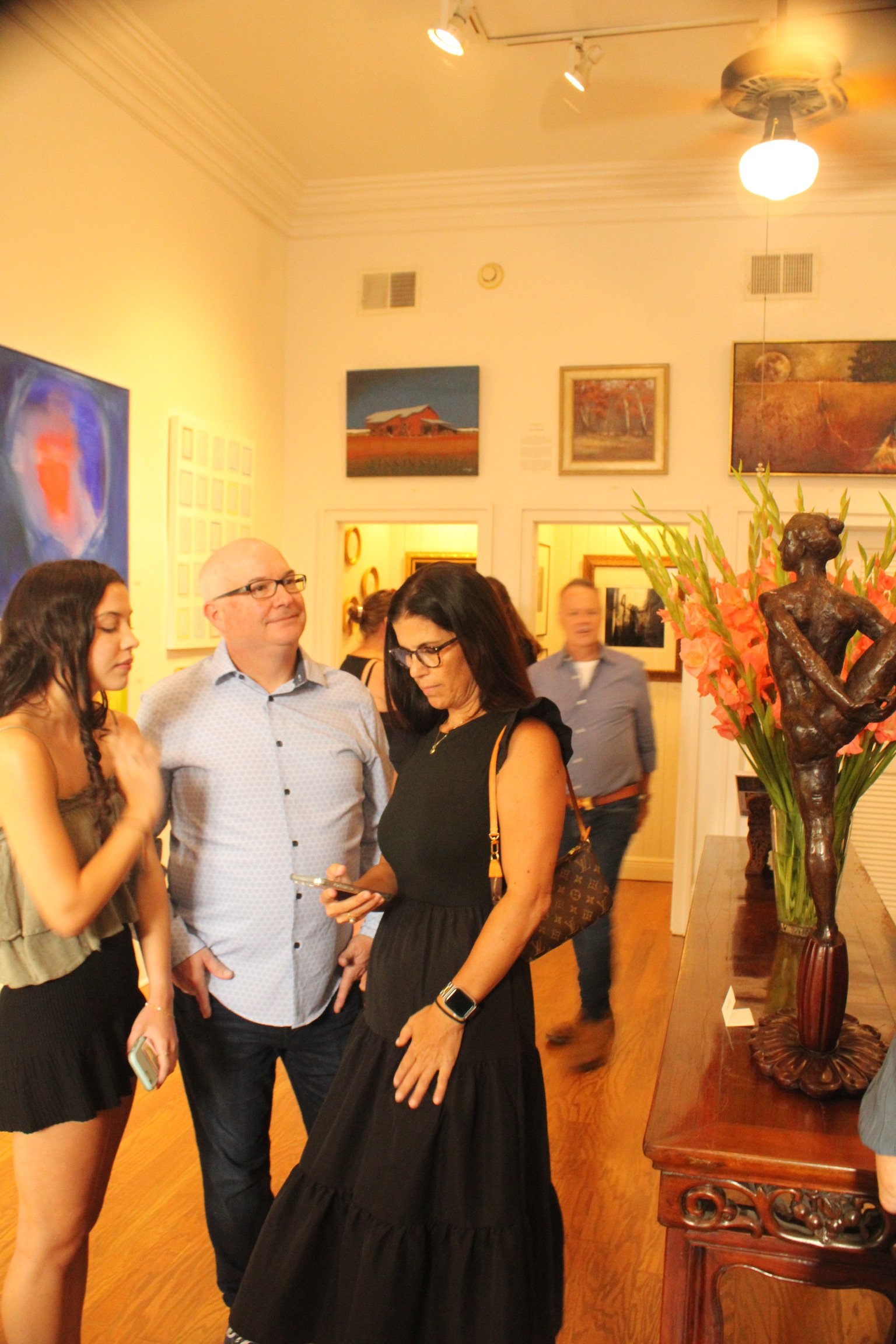 People gathered in an art gallery, looking at paintings and sculptures on display.