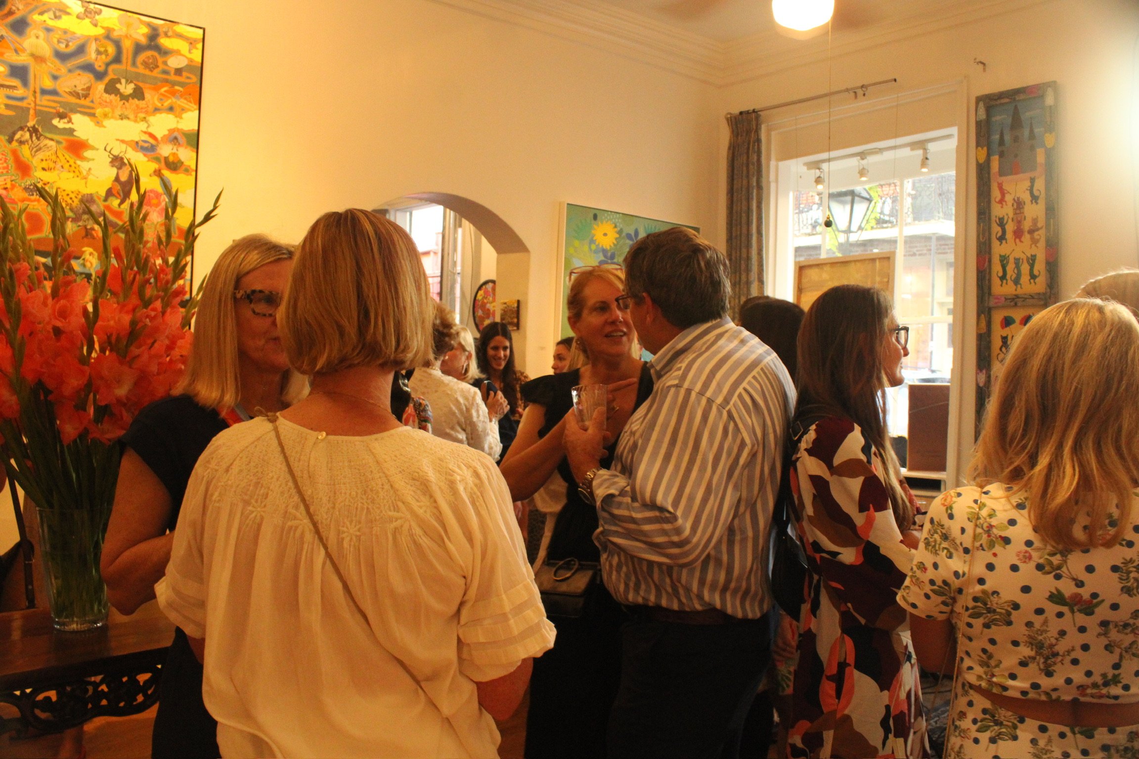 People gathered in a room with colorful artwork on the walls, engaged in conversation at what appears to be a social event or gathering.
