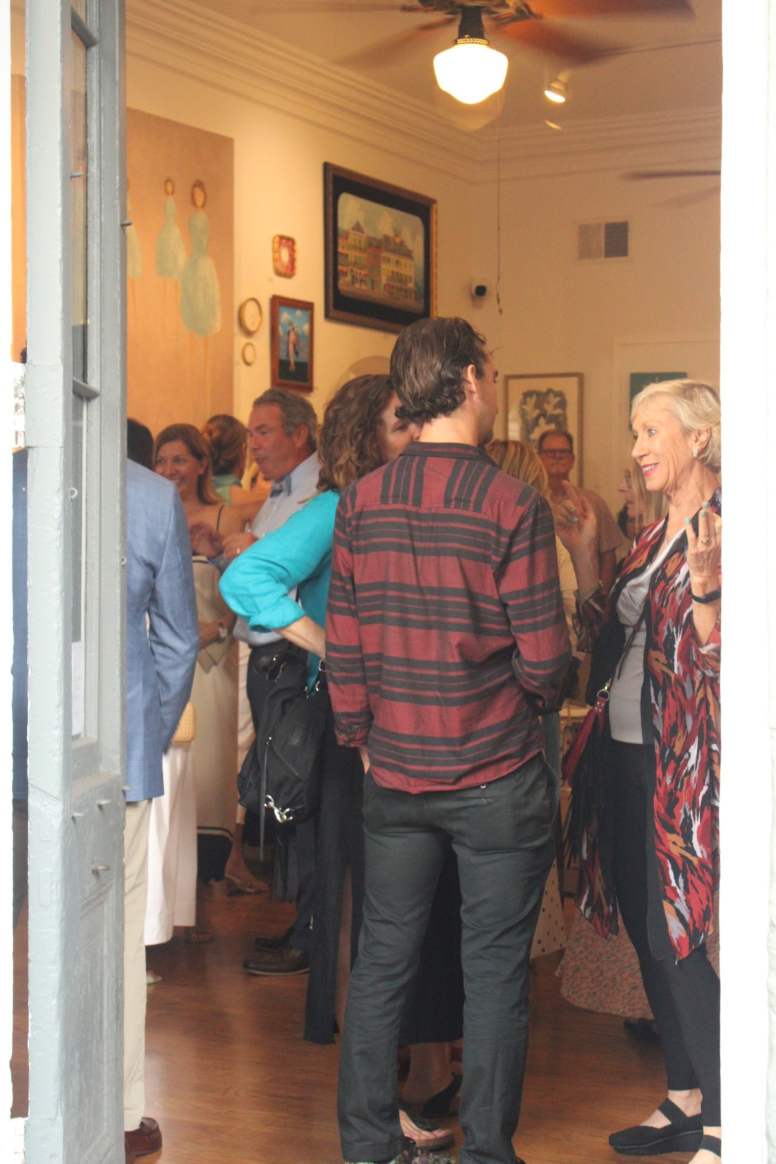 People socializing at an art gallery or exhibit, with paintings on the walls and wooden flooring.