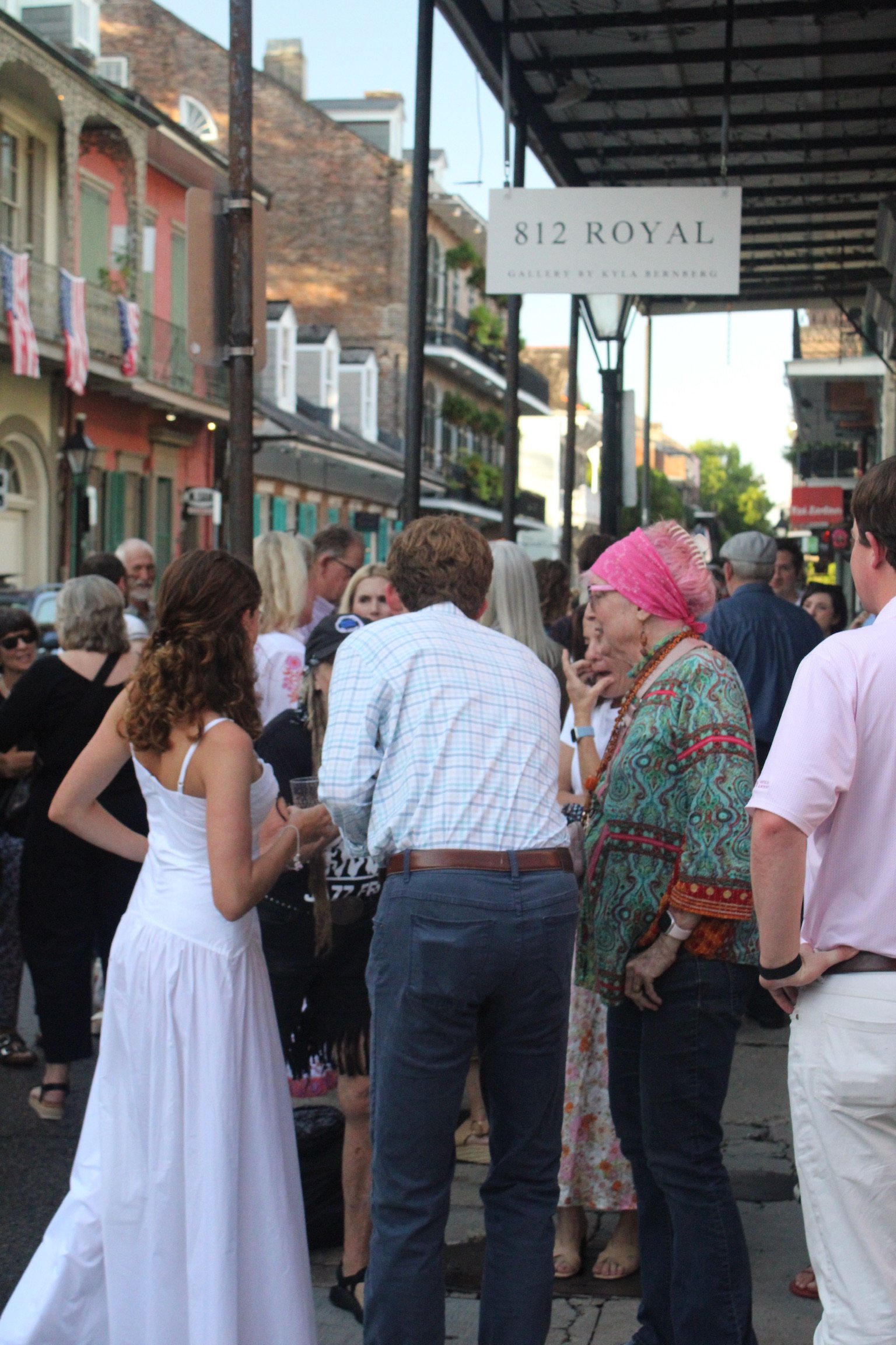 Crowd of people gathered on a city street with colorful buildings and a sign that reads '812 Royal Gallery & Cellar Dining'