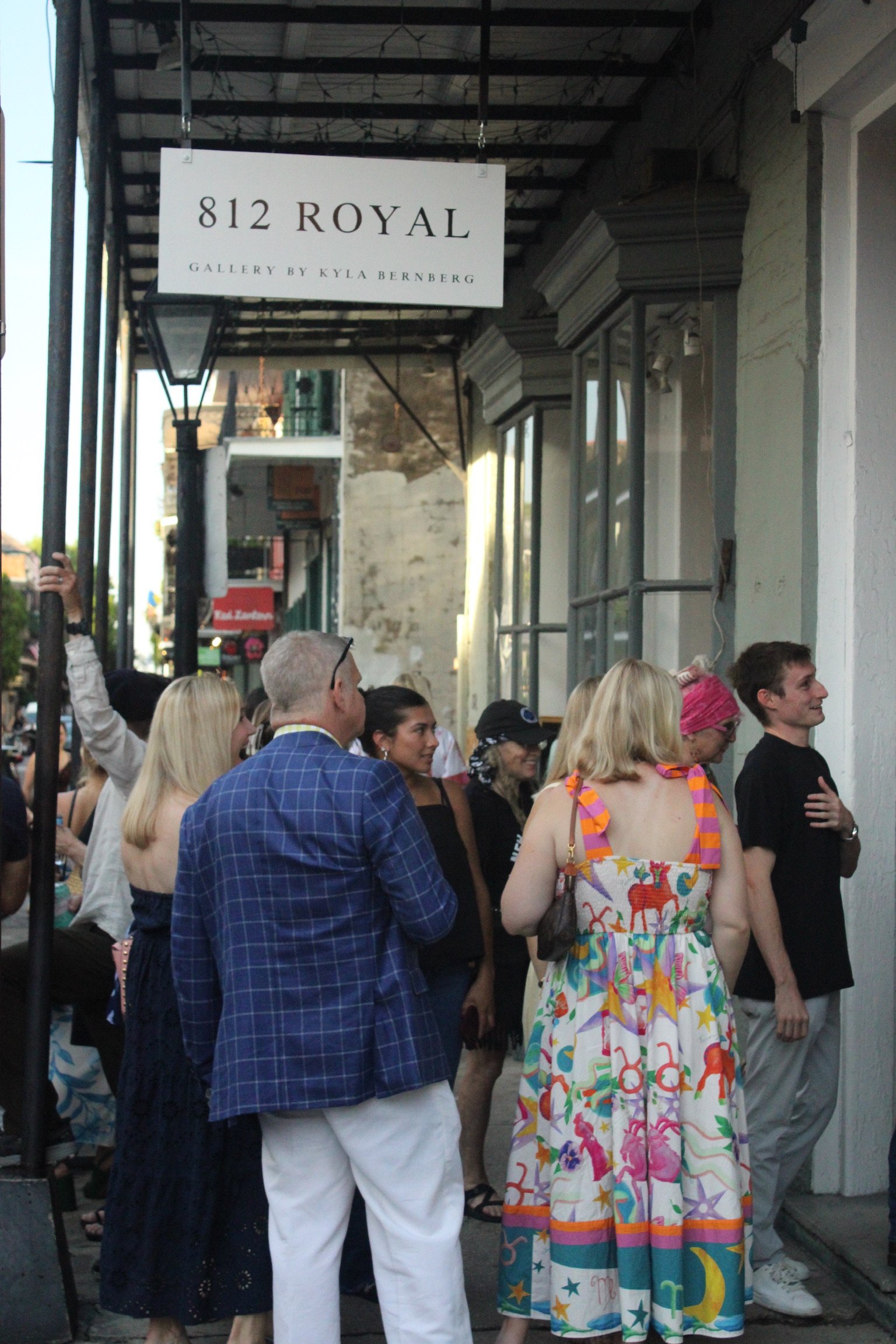 Crowd of people standing outside a building with a sign that reads '812 Royal, Gallery by Kyla Bernberg'.