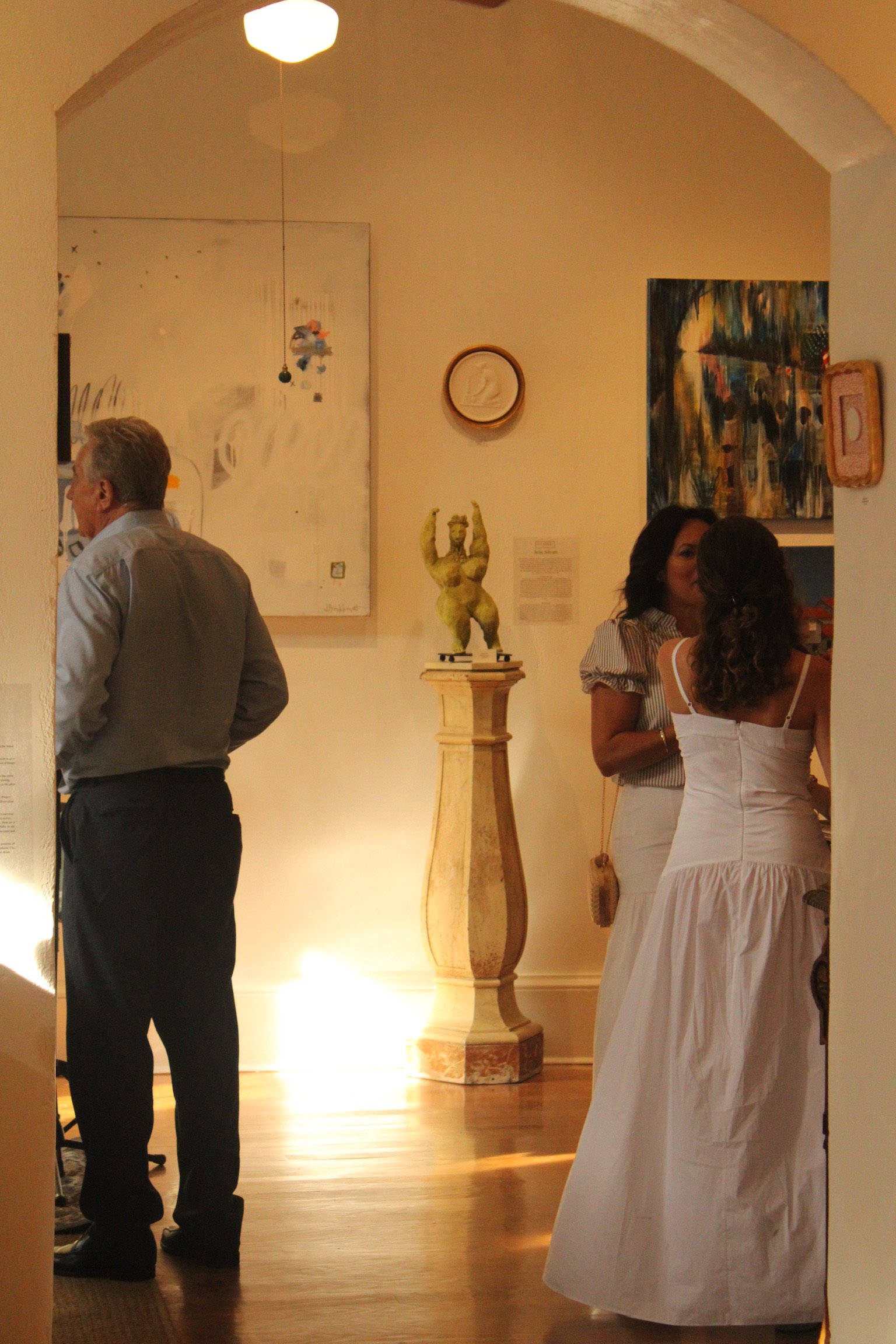 People socializing at an art gallery with paintings, sculptures, and warm lighting.