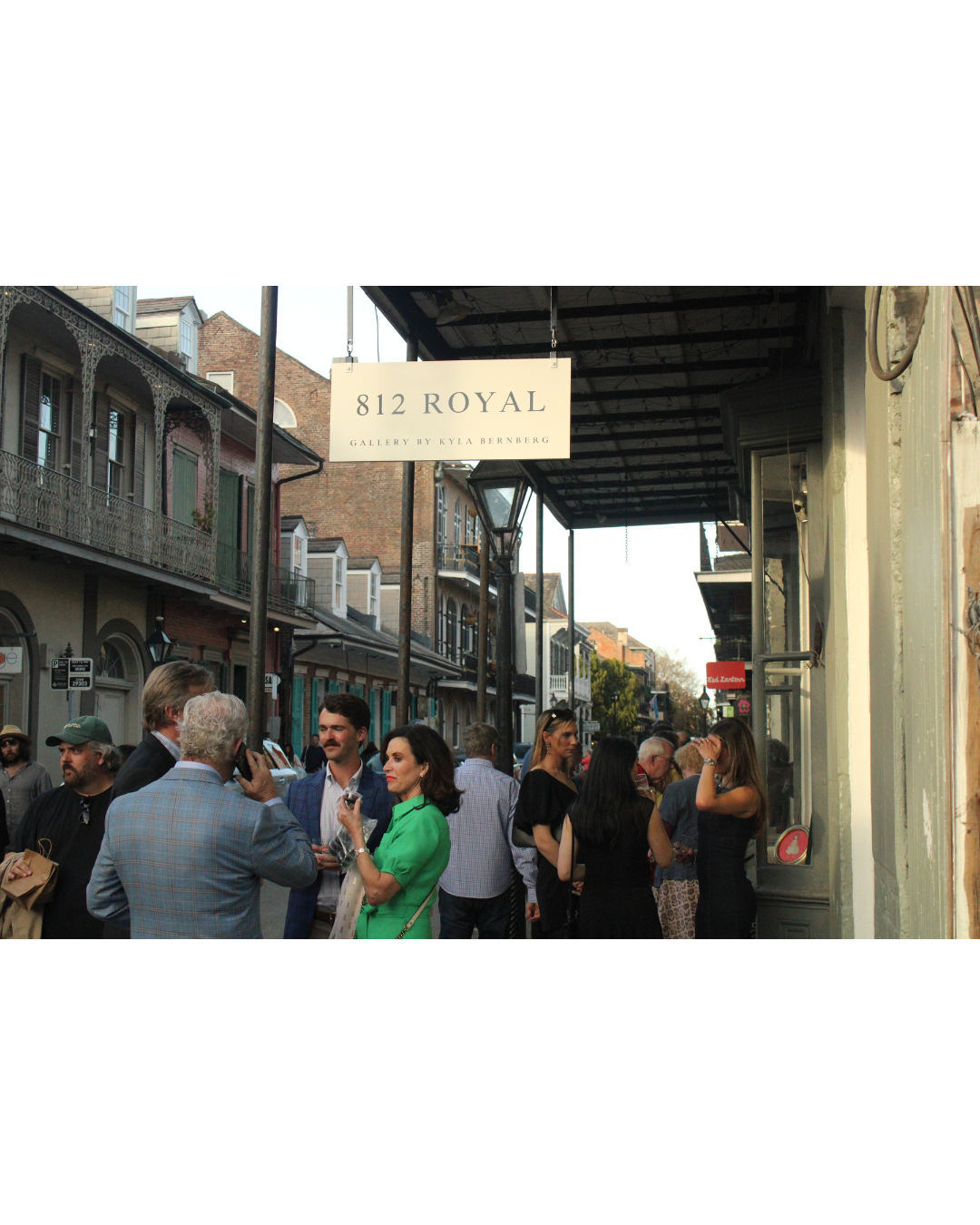 People gathered outside a gallery on a busy street with historic buildings, under a sign that reads '812 Royal, Gallery by Kyla Berenberg'.