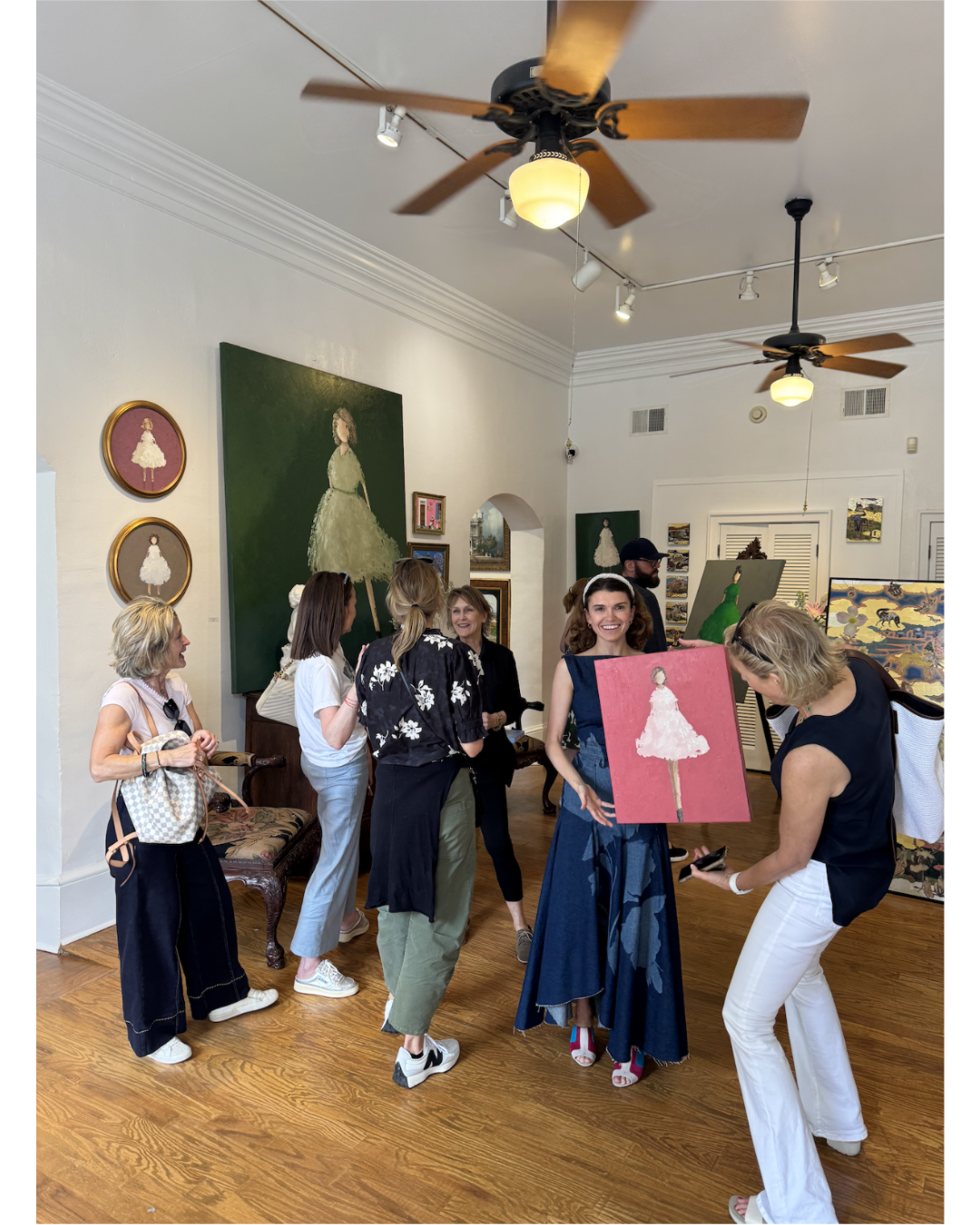Women viewing and discussing artwork at an art gallery, with paintings of girls in dresses on the walls.