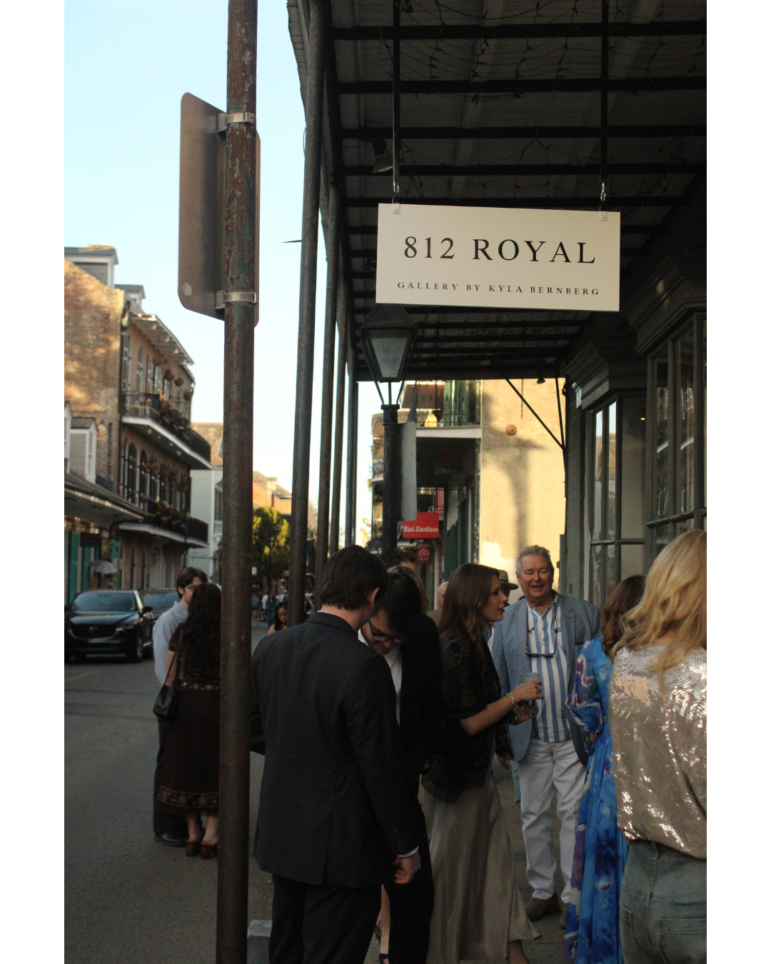 People standing on a sidewalk in front of a gallery with a sign that reads '812 Royal Gallery by Kyla Bernberg' in an urban area.