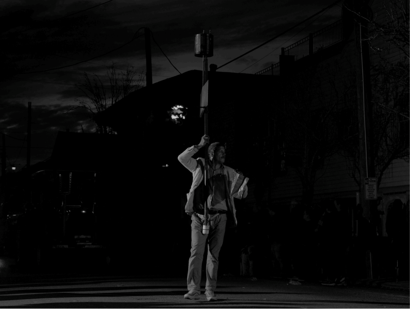 A person holding a pole with a flag or banner at night on a city street, with dark sky and streetlights in background.