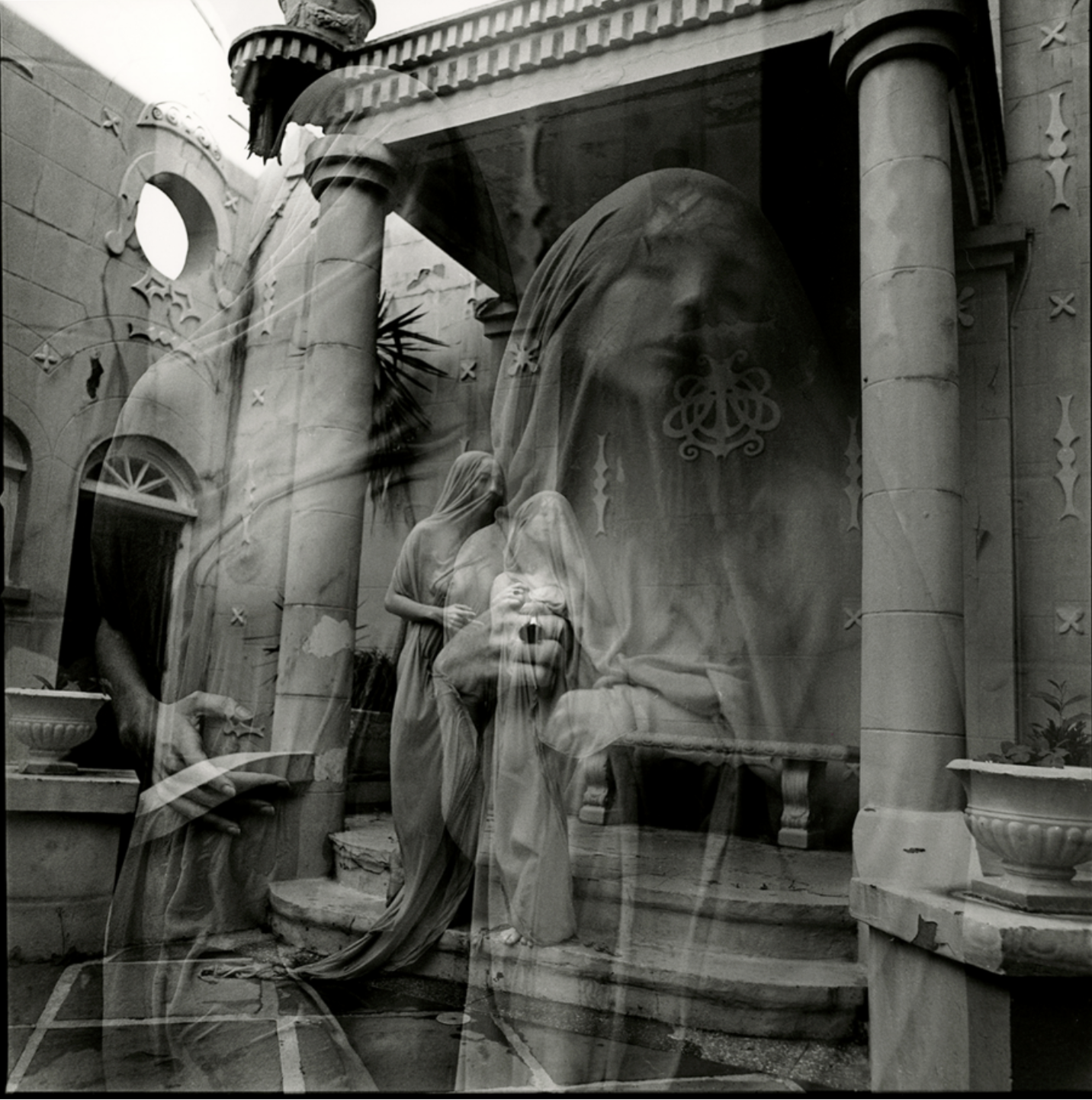 Black and white photo of a religious sculpture scene, showing a woman in a headscarf holding a baby, another woman standing nearby, with architectural columns and details in the background.
