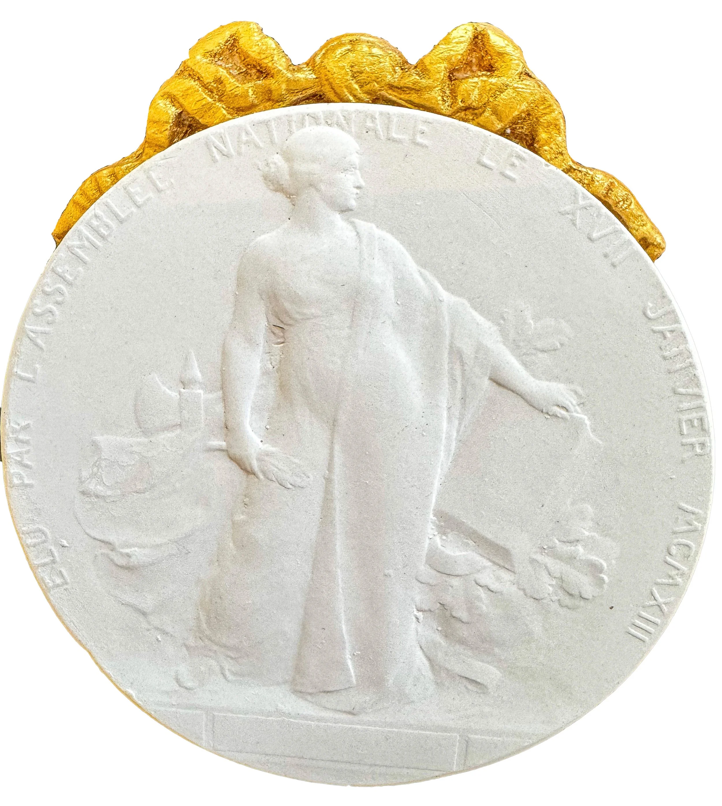 A close-up of a white coin with an embossed portrait of a woman wearing a crown, indicating it is a British coin. The coin features raised text and a patterned rim.