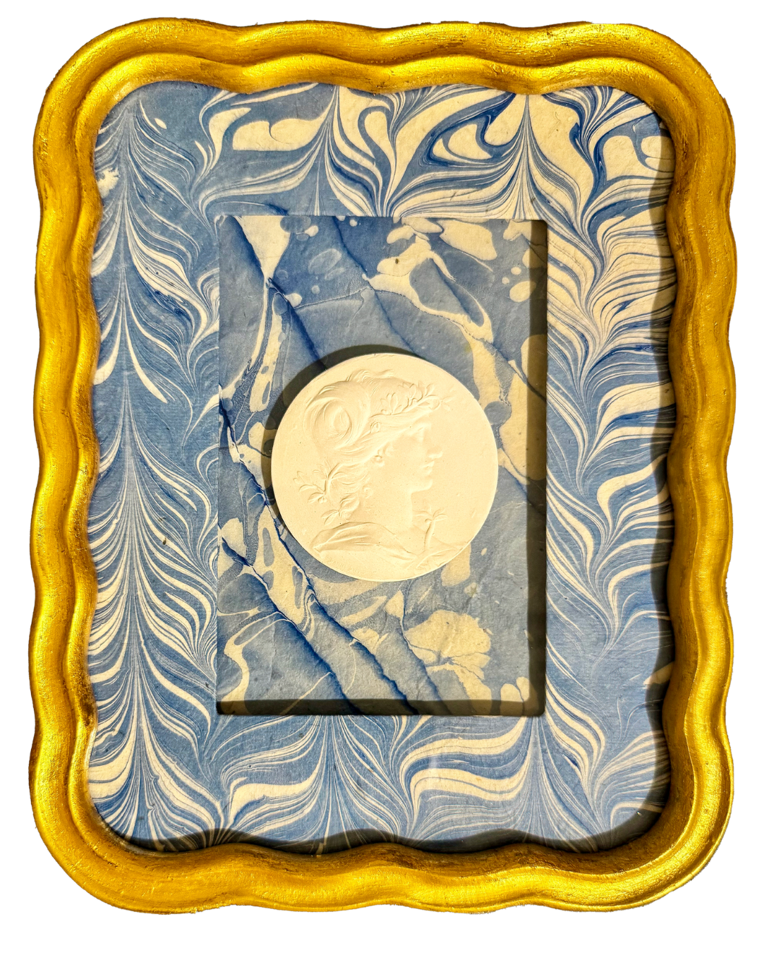 Marbled blue and white decorative paper with a framed embossed profile of a woman's face and hair, in a gold ornate frame.