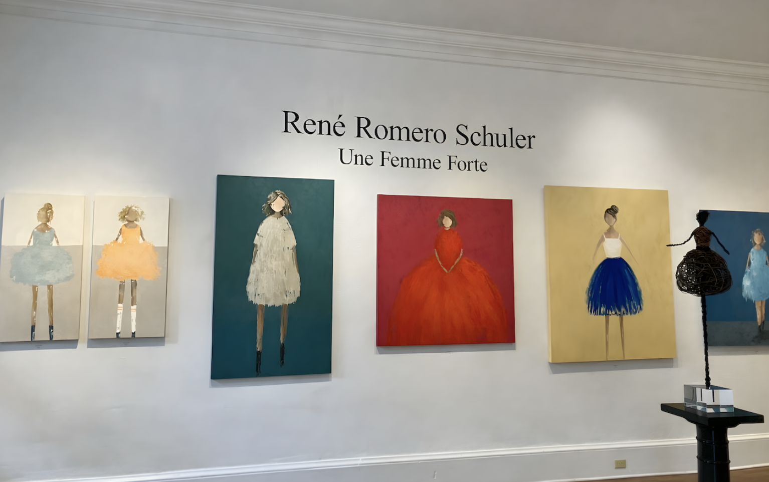 Exhibition wall displaying six paintings of women in colorful dresses, with the artist's name René Romero Schuler and title 'Une Femme Forte' written above.