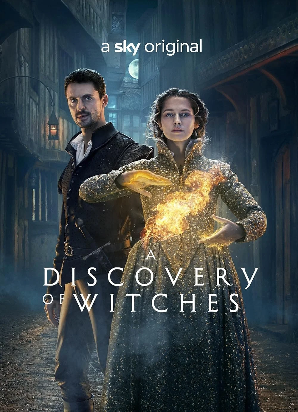 Promotional poster for 'A Discovery of Witches' featuring a man and a woman in period clothing, with the woman conjuring fire with her hand, set against a dark street scene with old buildings and a full moon.