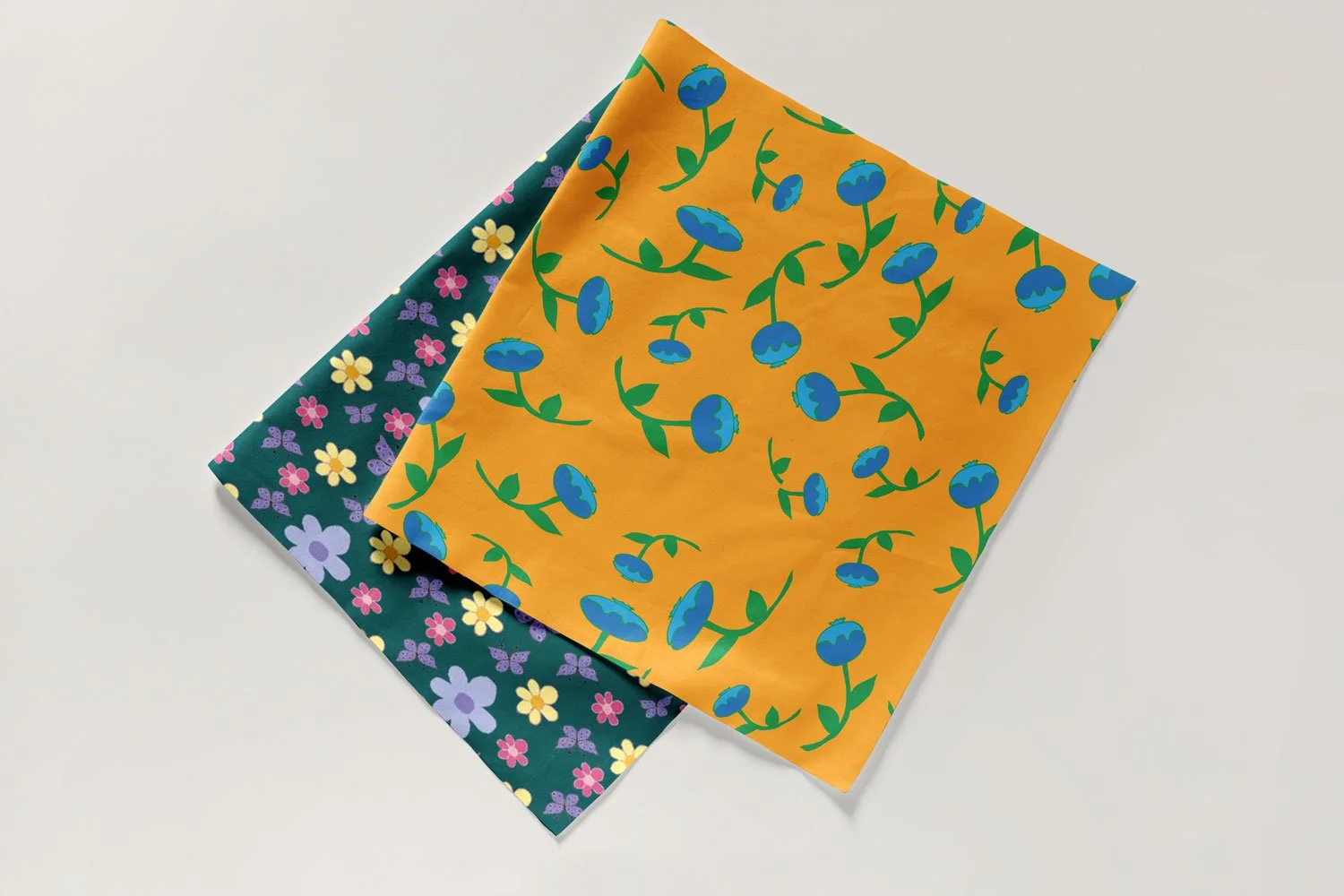 Nature-inspired surface pattern designs of blueberries on a yellow background and flowers on a dark green background.