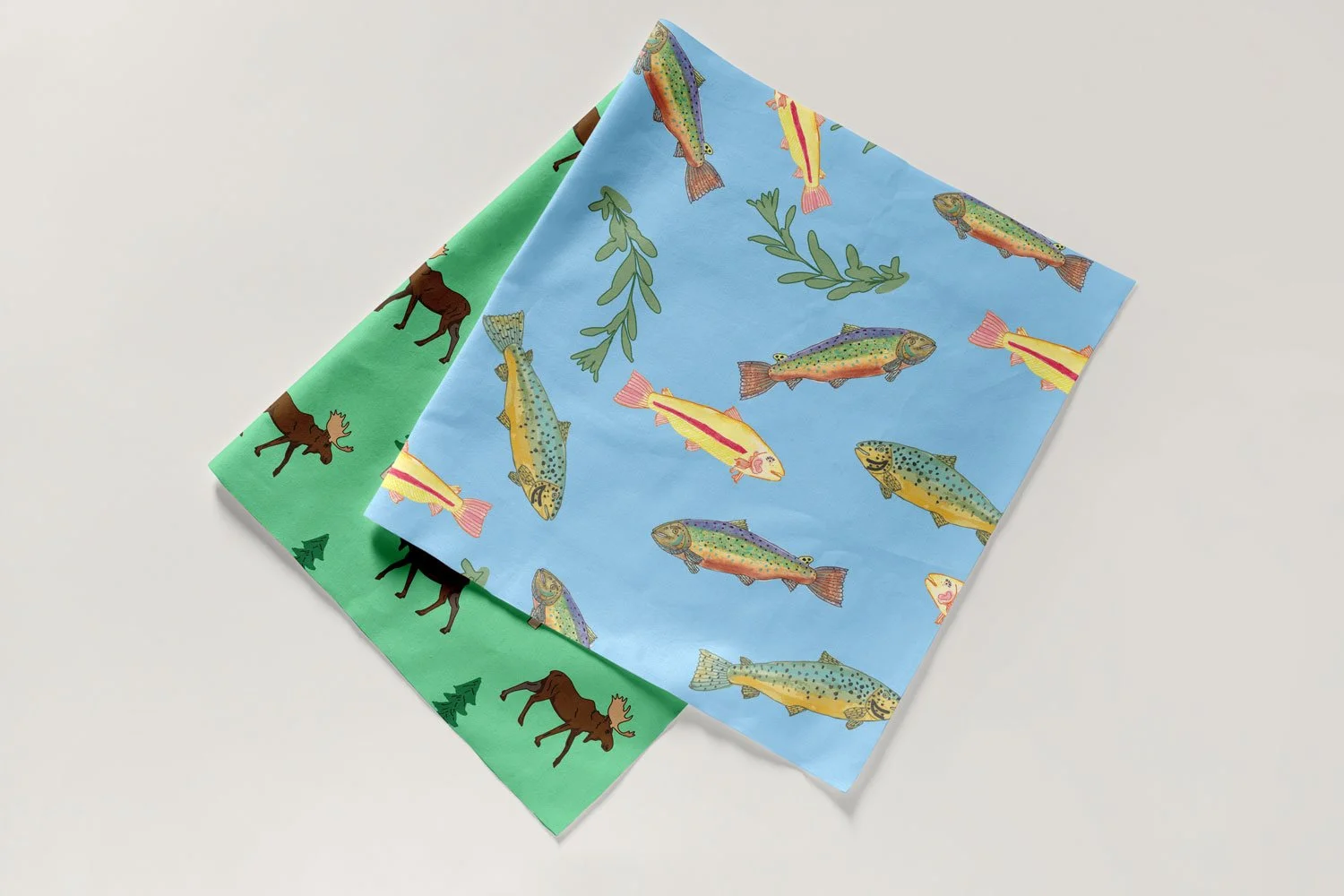 Two colorful fabric swatches with outdoor nature motifs, featuring fish on a blue background and moose and trees on a green background.