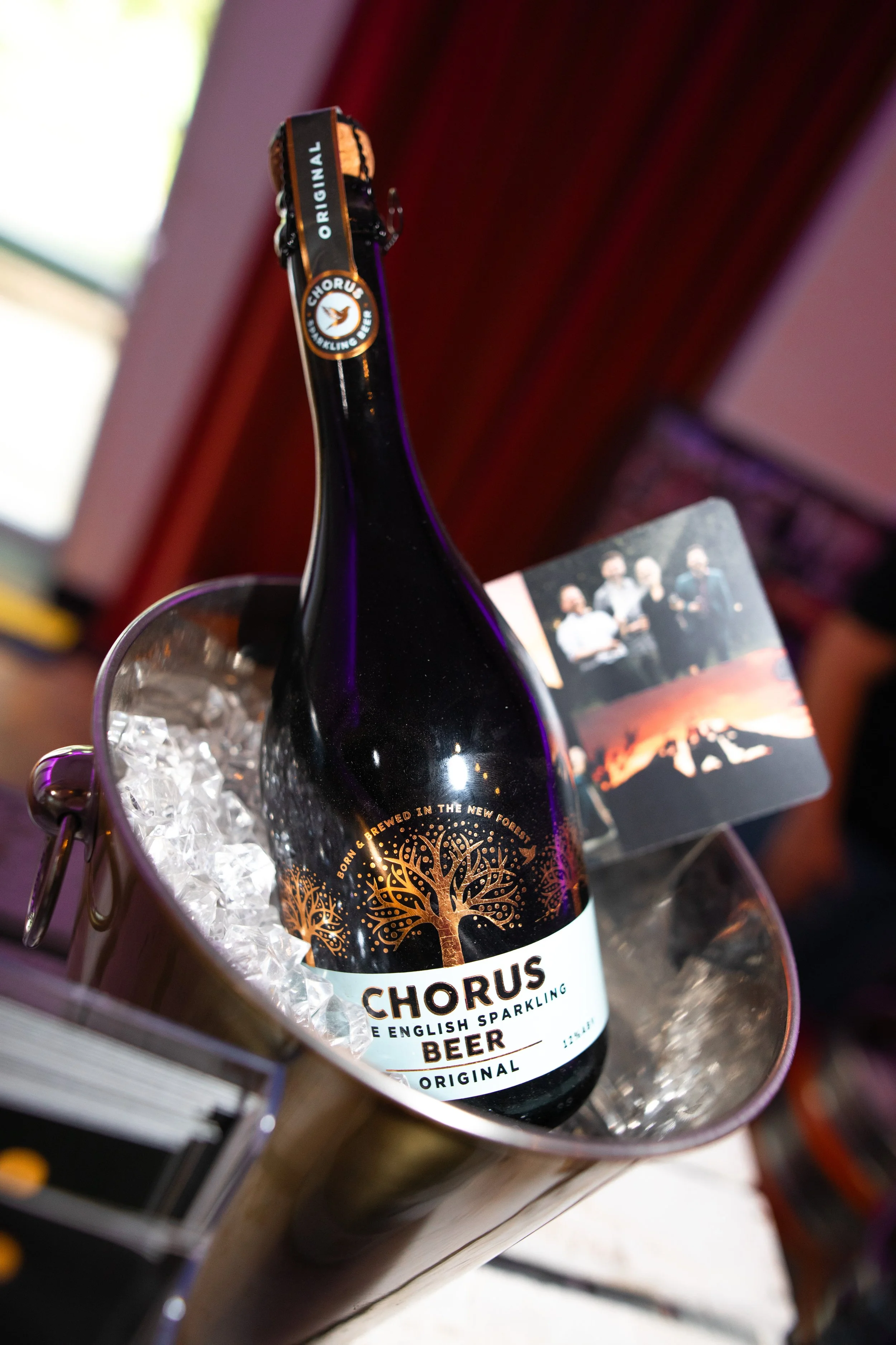 A bottle of Chorus English sparkling beer in a metal bucket filled with ice cubes, with a photo of a band on the side.
