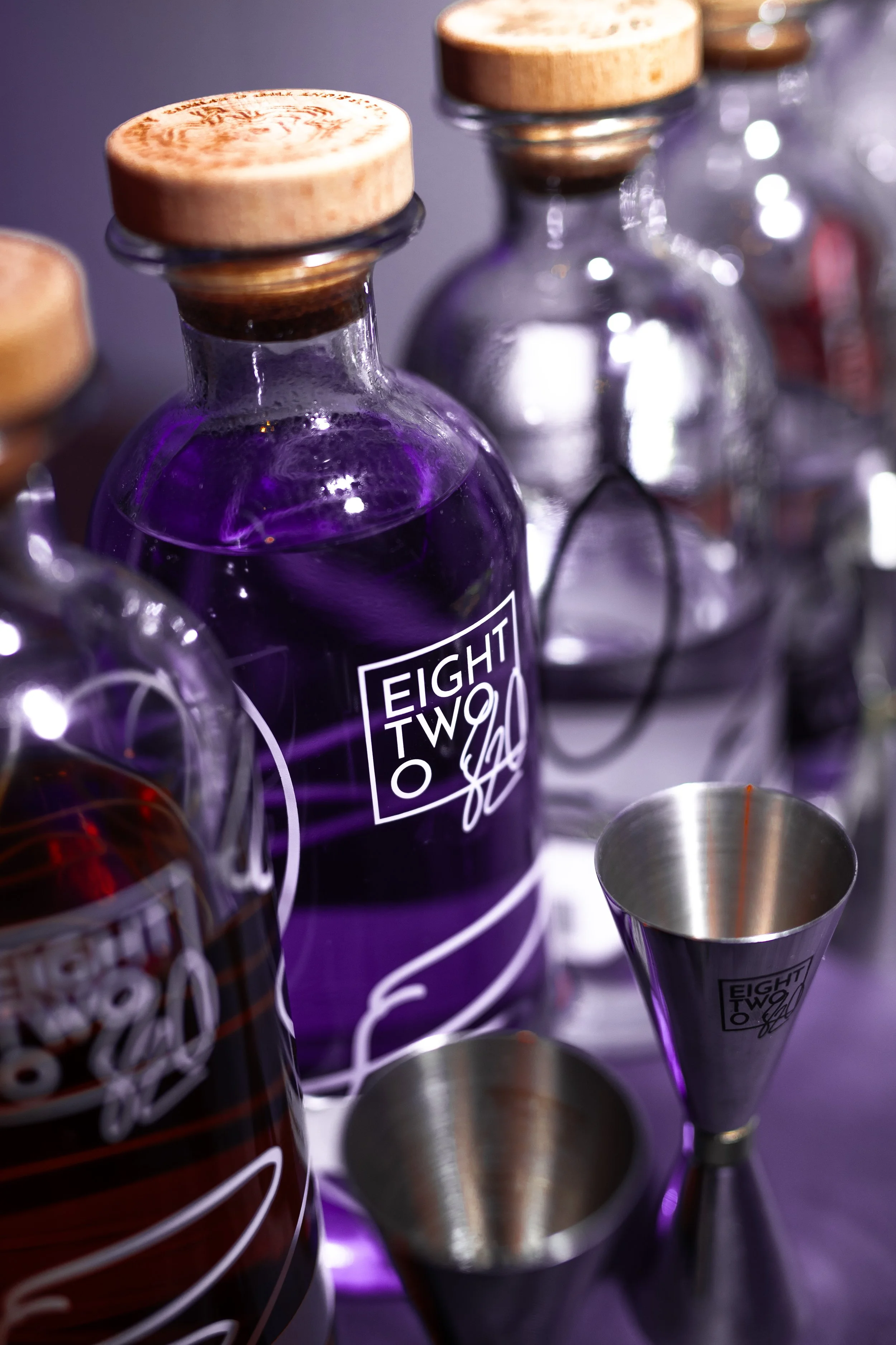 Close-up of several empty wine glasses and bottles, with a focus on a purple-tinted bottle that has a label reading "EIGHT TWO TO".