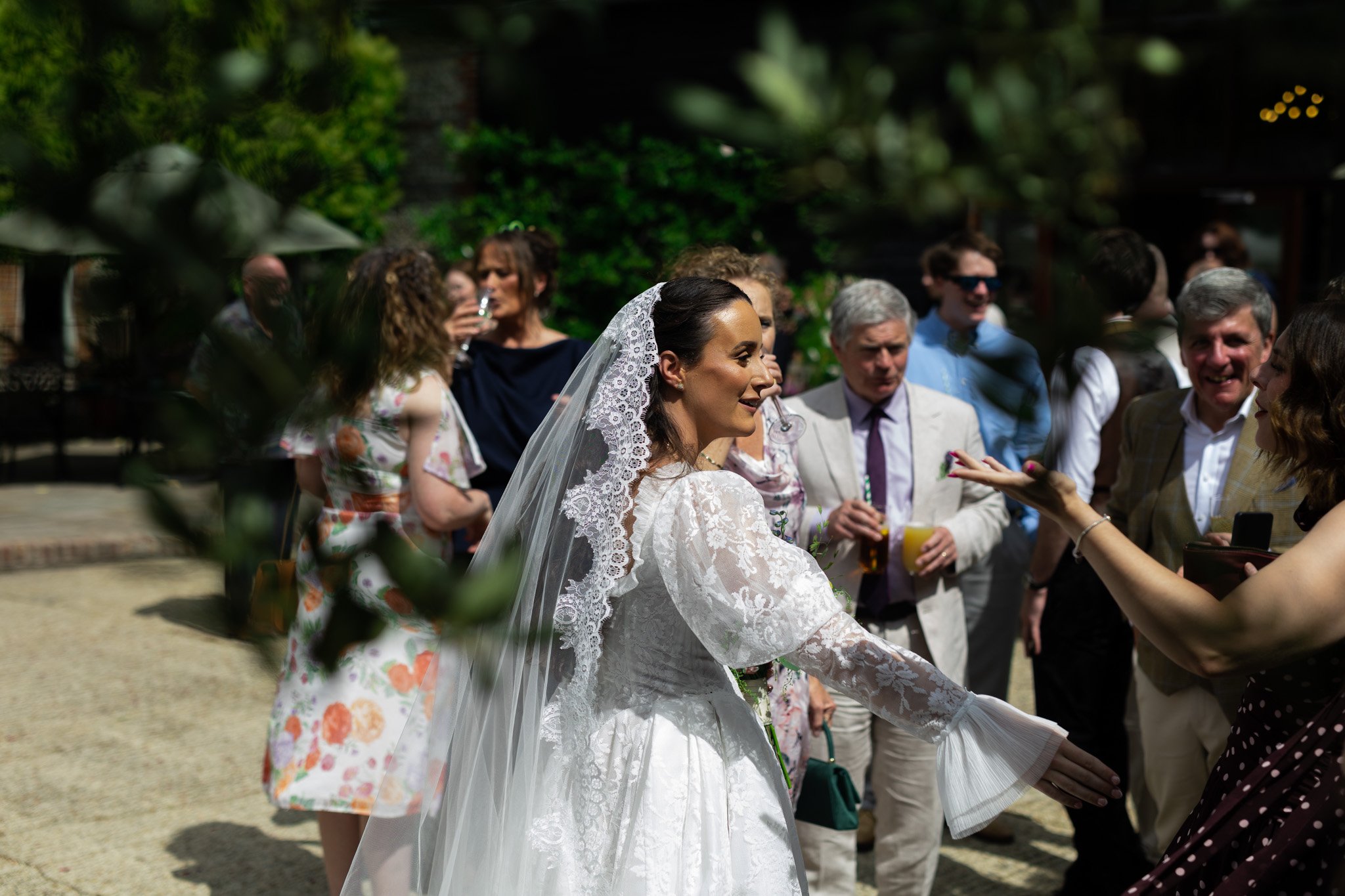 A bride in a white veil greets guests after the ceremony at the upwaltham barns courtyard