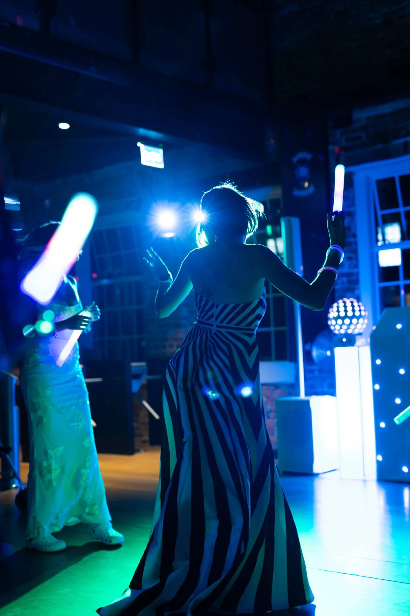 People dancing in a dark room with vibrant blue and green lights, some wearing costumes including a person in a long, striped dress.