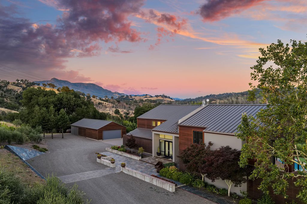 Modern house with a metal roof in a scenic landscape with mountains and colorful sunset sky.