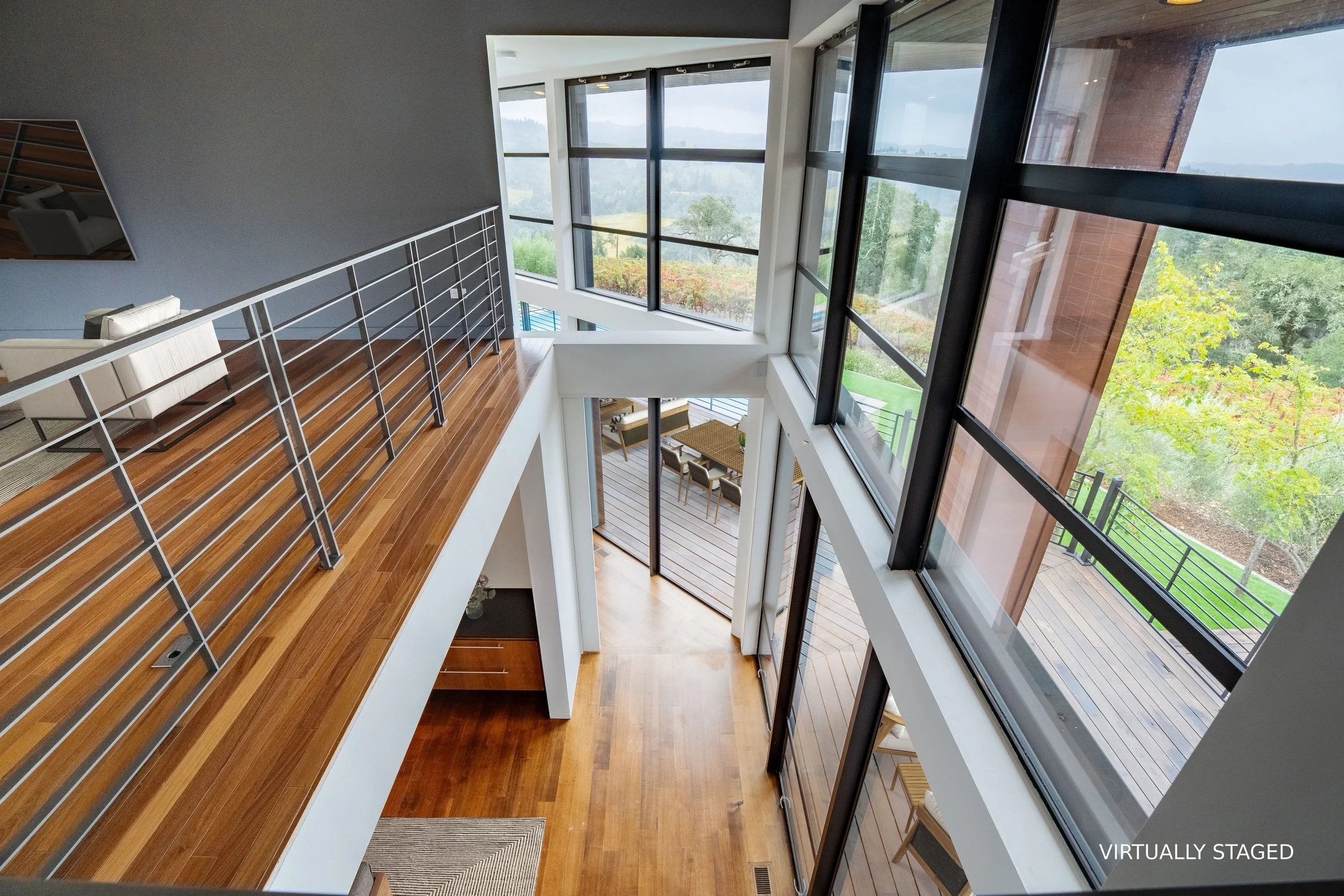 Interior view of a modern multi-story home with large windows, wooden flooring, and outdoor deck space, showcasing a scenic landscape.