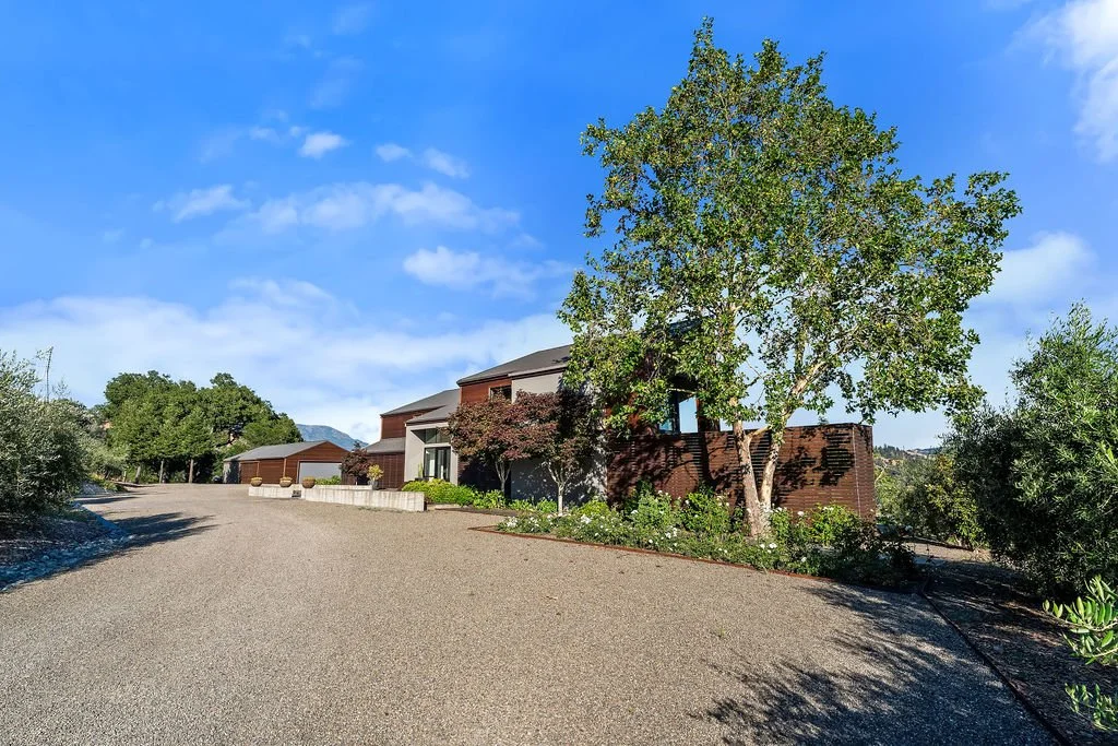Residential house with a large tree in a landscaped yard on a sunny day.