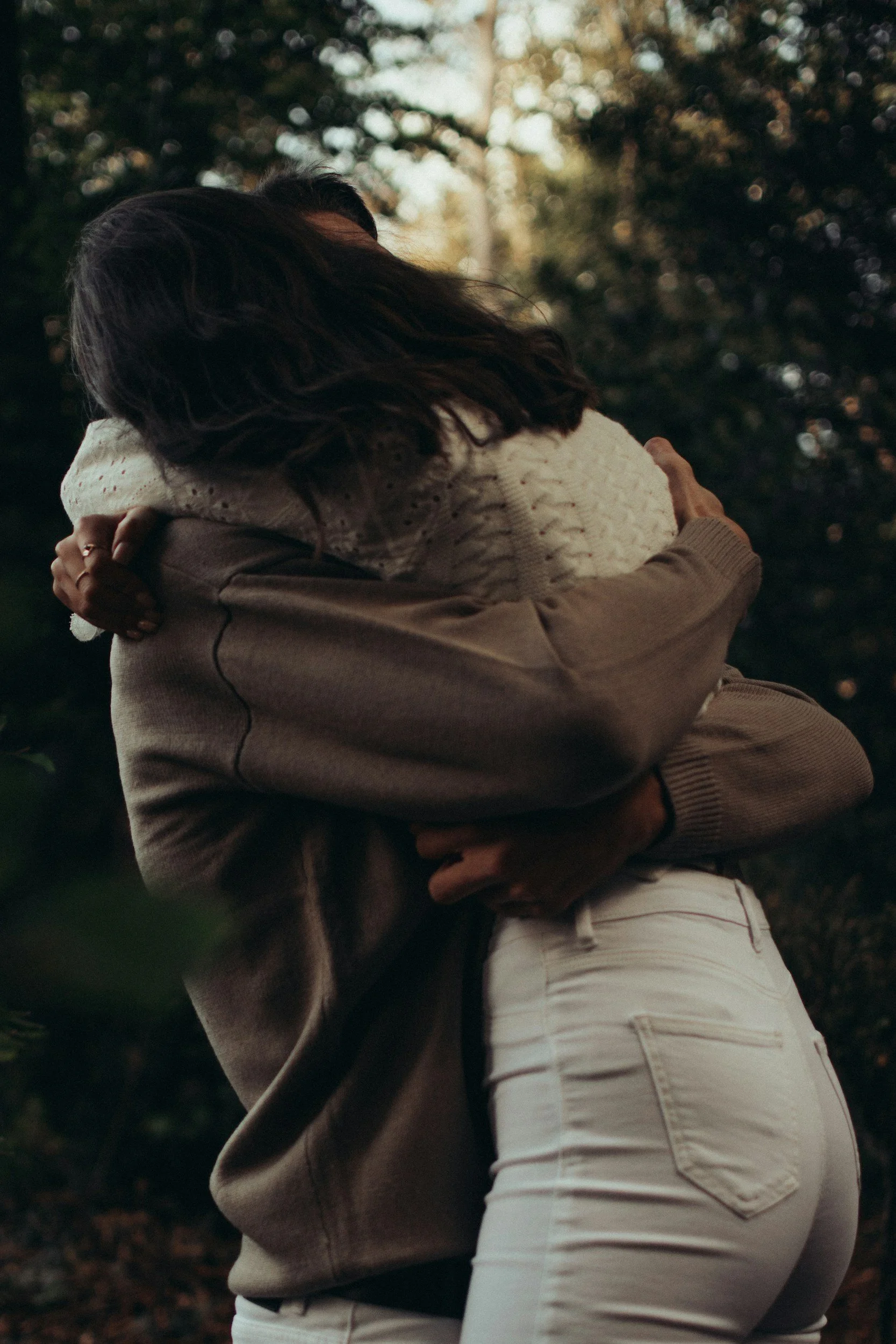Two people hugging outdoors during sunset, with trees in the background.