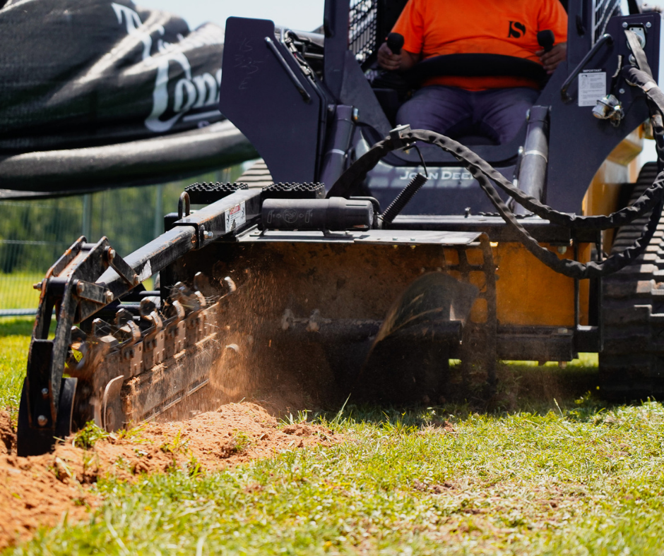 A person operating a skid steer loader with a flail mower attachment, cutting grass on a field.