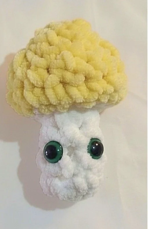 a crochet yellow and white mushroom pop it with green eyes.
