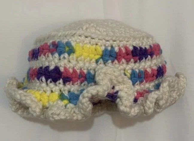 Colorful crocheted hat with rainbow-colored stripes and a ruffled brim.