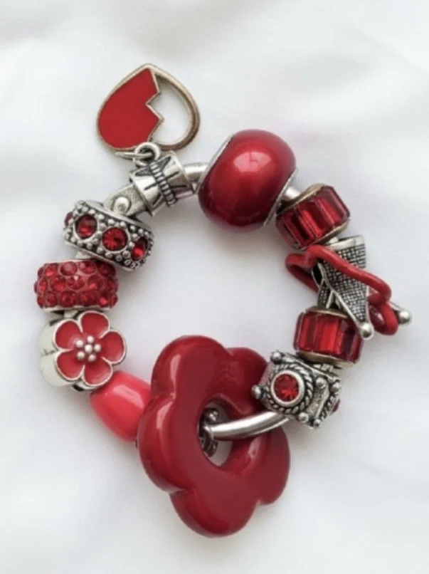 Red and silver charm bracelet with various red beads and decorative charms, featuring a red heart theme.