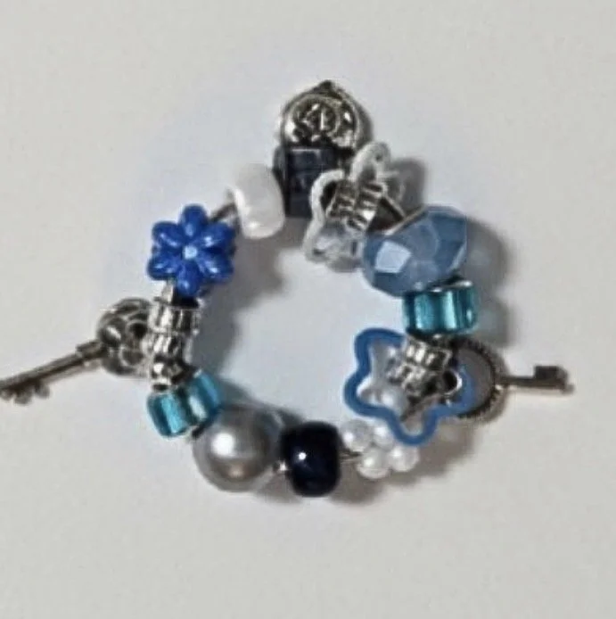 A charm bracelet with various beads in blue, white, turquoise, and silver, including flower, heart, and key charms.
