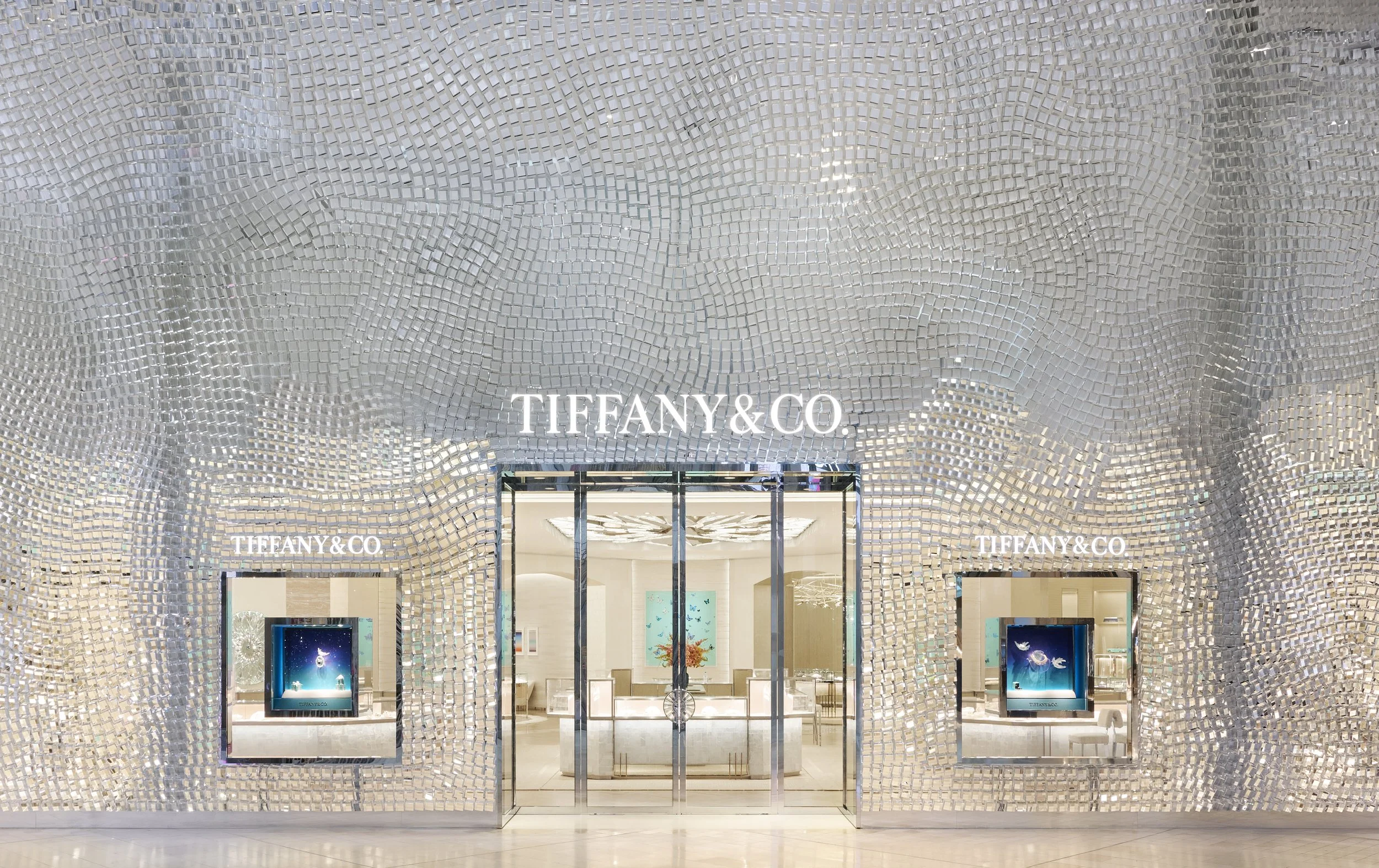 The exterior of a Tiffany & Co. storefront with a metallic, mosaic-style facade and illuminated signage.