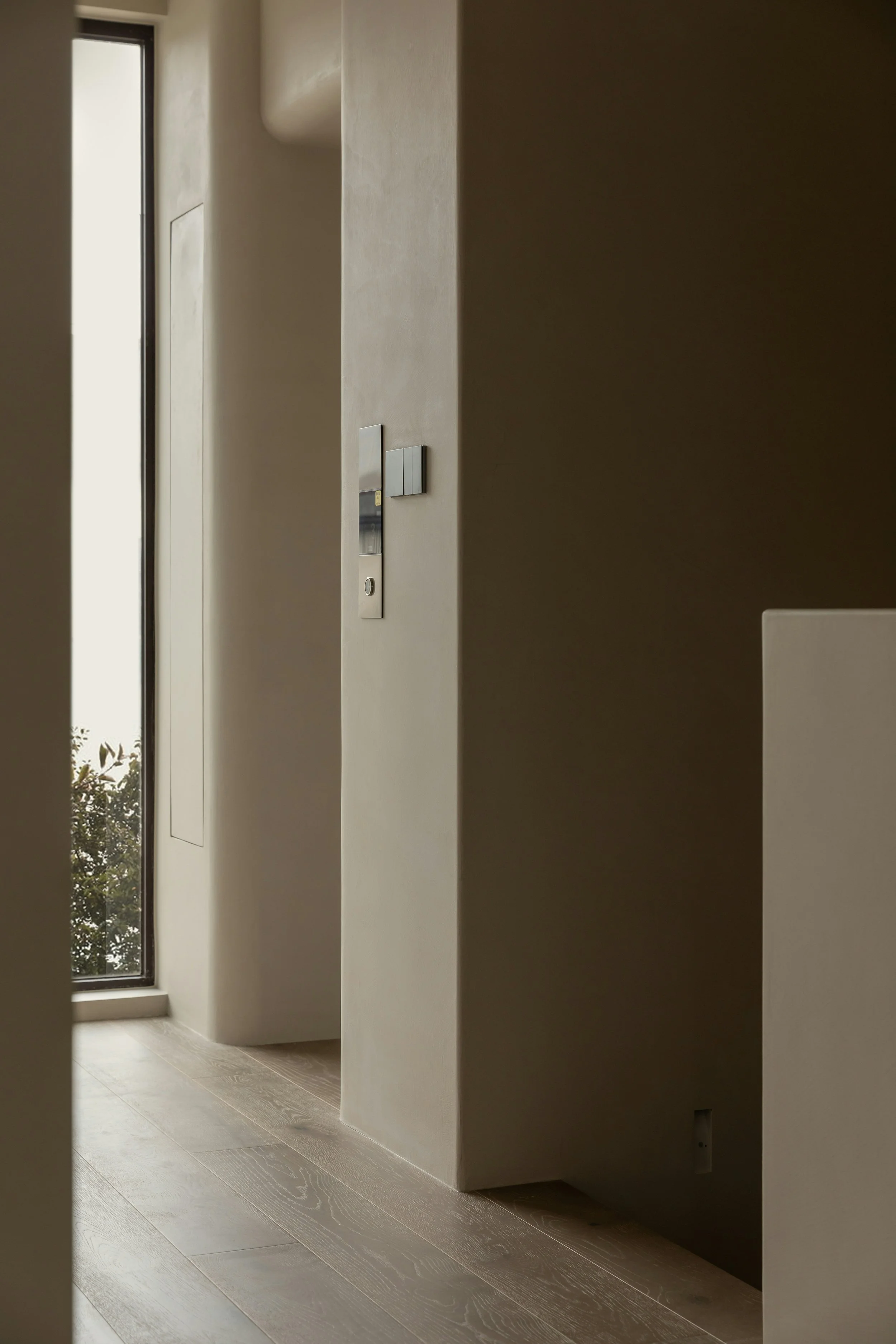Interior view of a modern room with a large window, a wall-mounted panel, and light-colored wooden flooring.