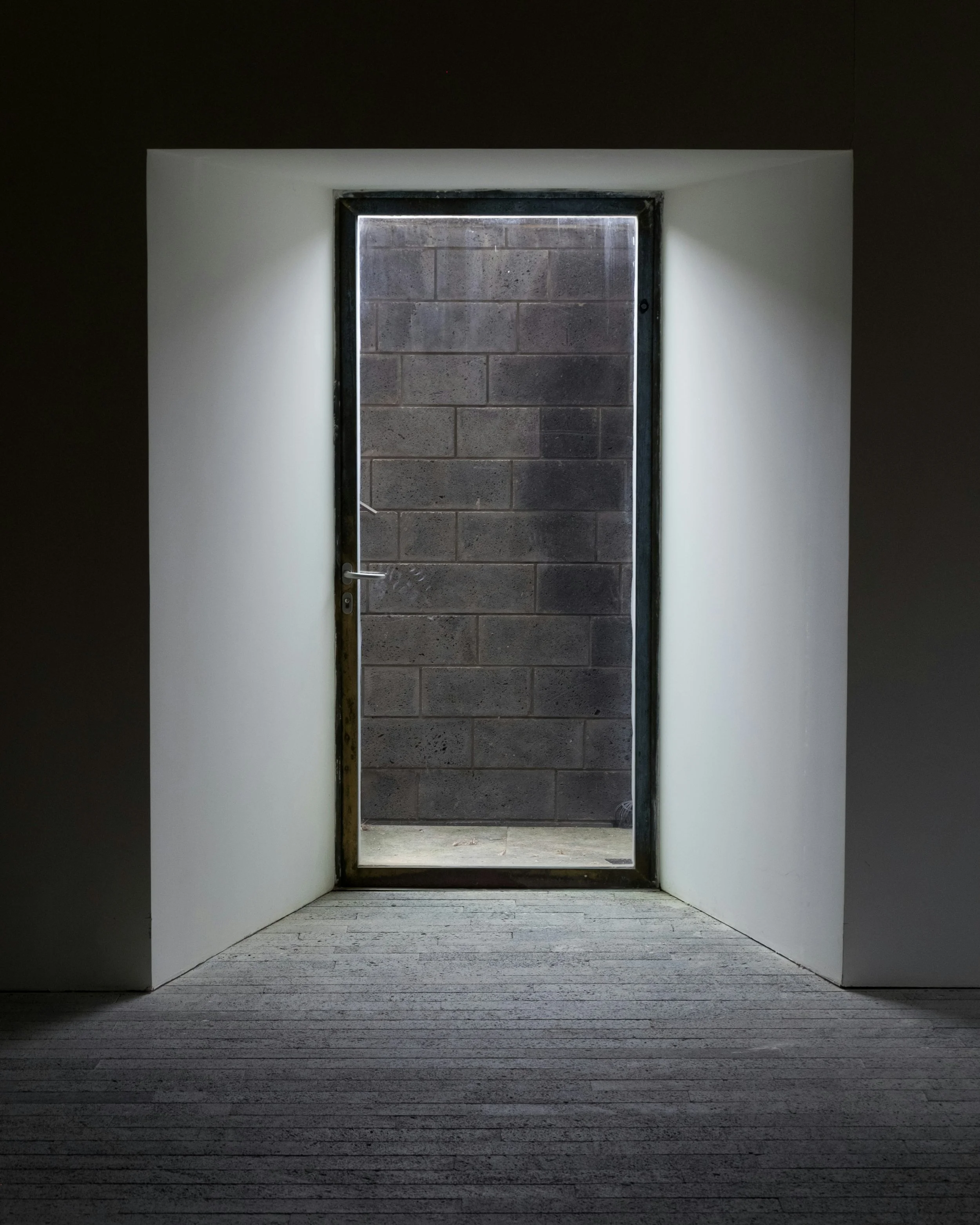 Open black door leads to a concrete block wall outside, with white walls and wooden flooring inside.