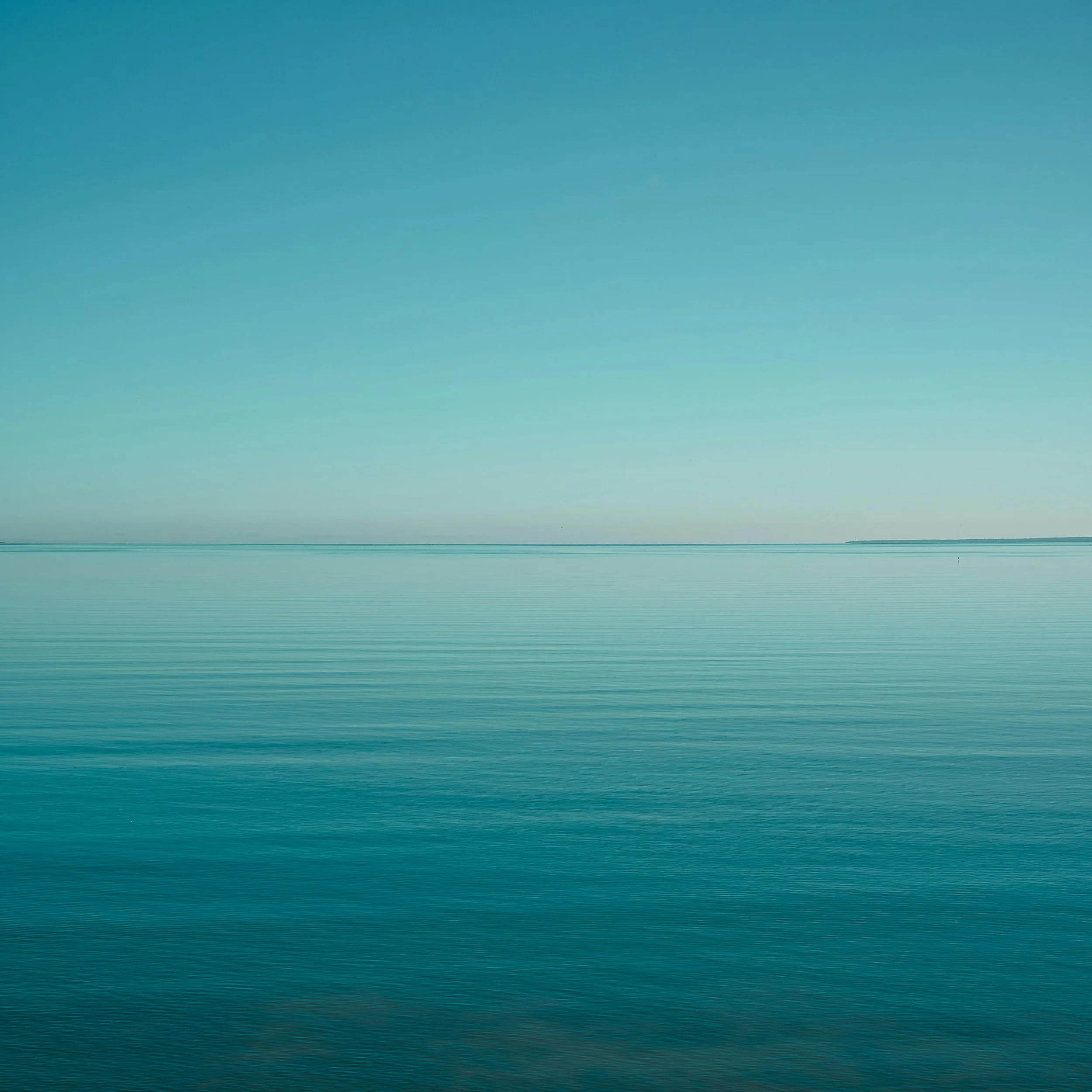 Blue sky above a calm body of water extending to the horizon.