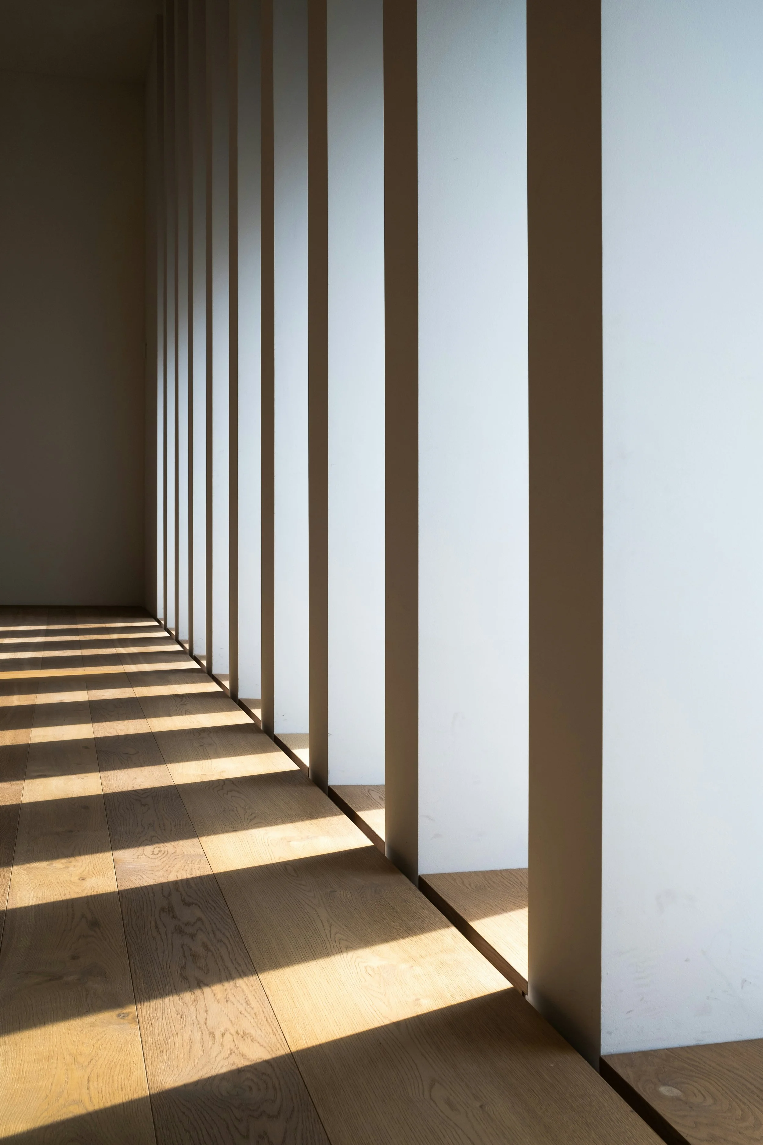 Sunlight casting striped shadows on wooden floor and white vertical panels in a modern interior space.