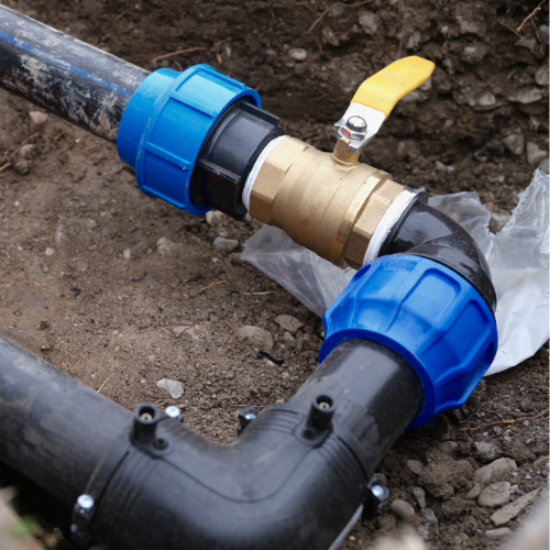 Close-up of a water valve attached to black plastic piping underground.