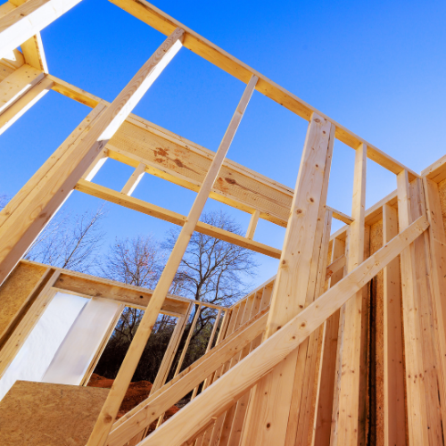 Wooden framing of a house under construction against a blue sky.