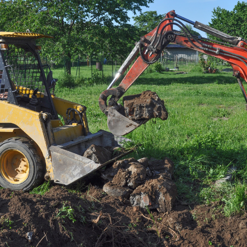 Excavator is lifting large rocks during land excavation in a grassy outdoor area.