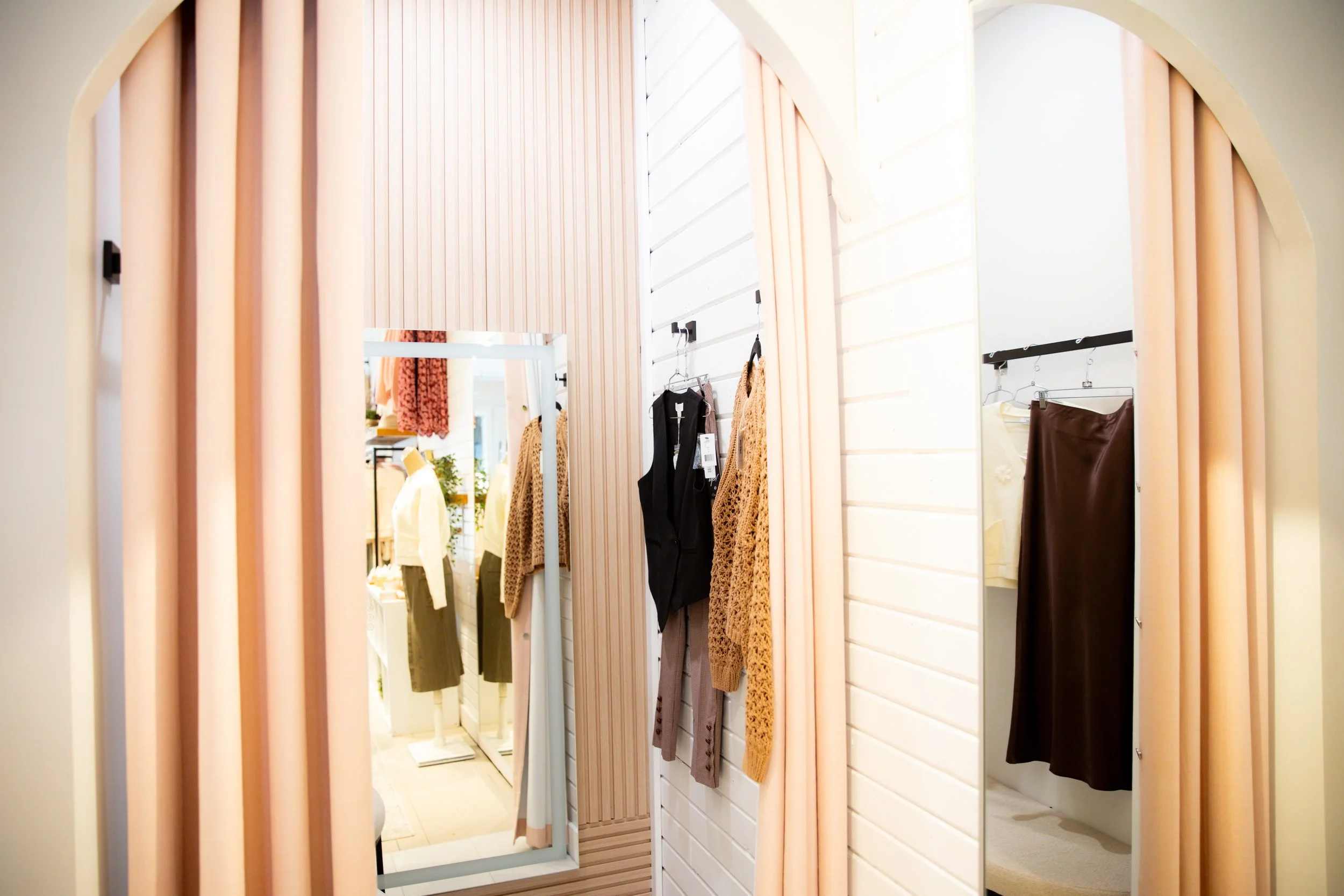 A fitting room with hanging clothes and a full-length mirror.