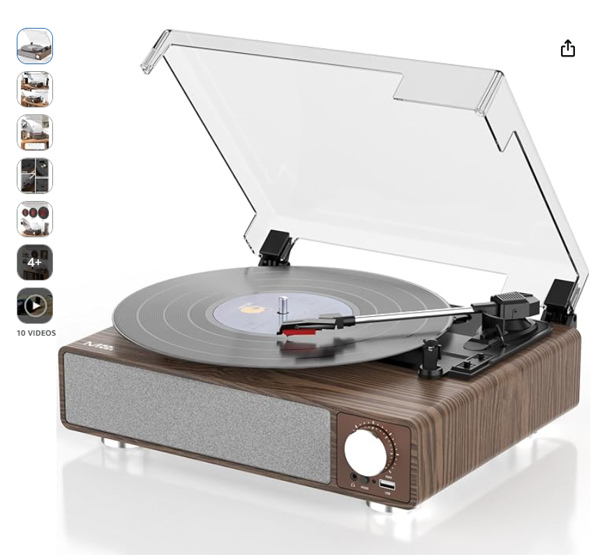 A vintage-style turntable with a wood finish, grey speaker, and a clear dust cover, playing a vinyl record.