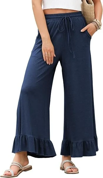 Woman wearing navy blue wide-leg pants with ruffled hems and a white crop top, holding a straw bag, with sandals and bracelets.